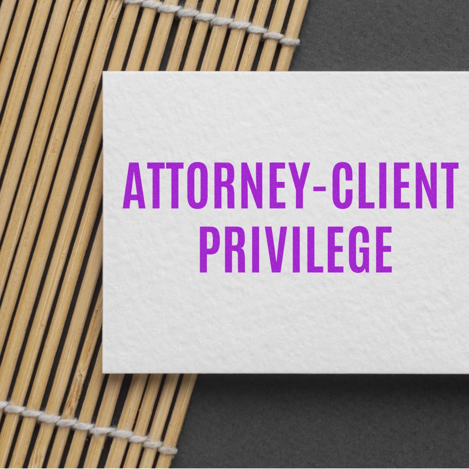 Slim Pre-Inked Attorney-Client Privilege Stamp used on a white card with purple text, placed on a bamboo mat background.