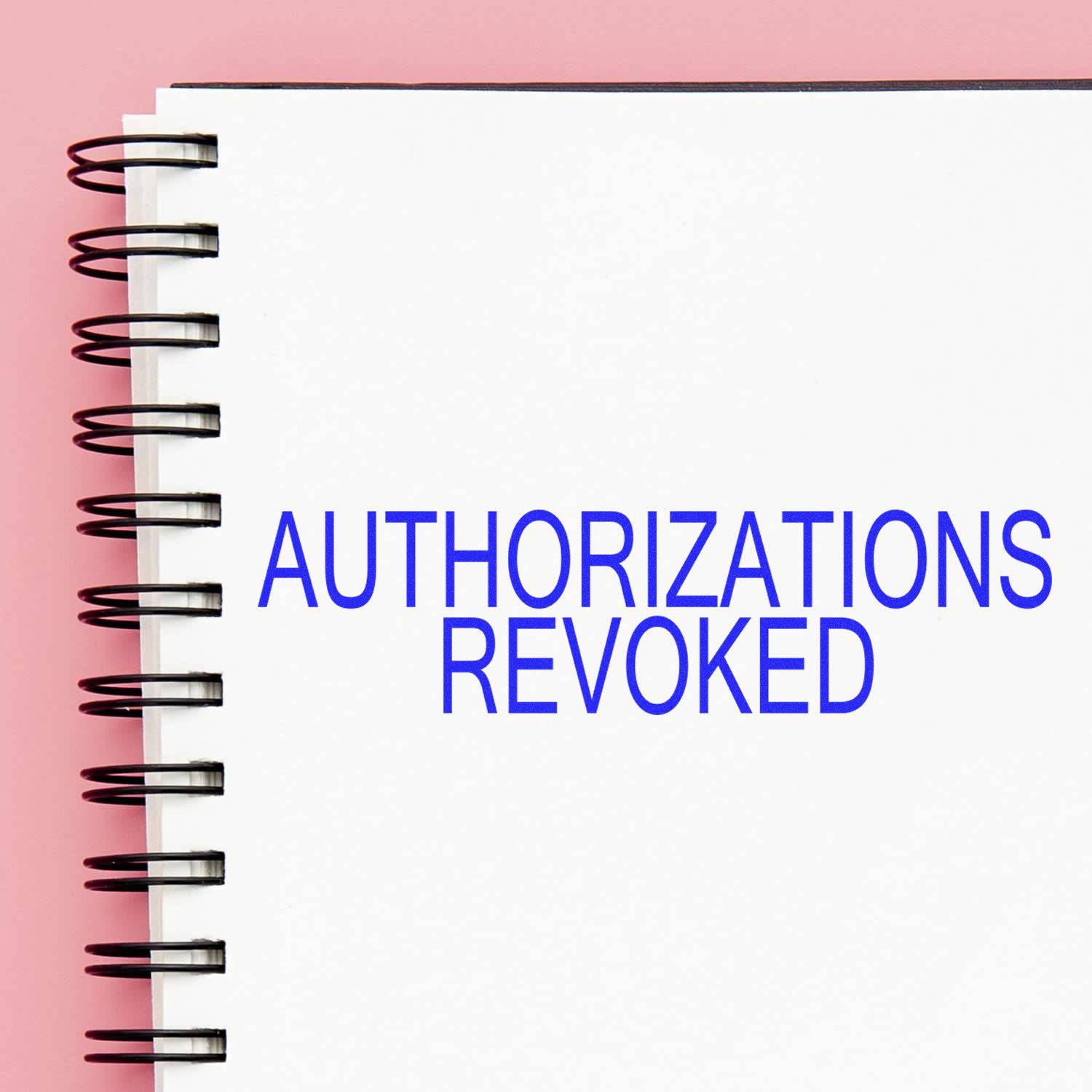 Large Pre-Inked Authorizations Revoked Stamp used on a white notebook with a pink background.