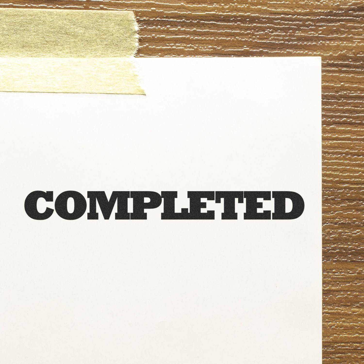 Large Self Inking Bold Completed Stamp marking COMPLETED on a white paper taped to a wooden surface.