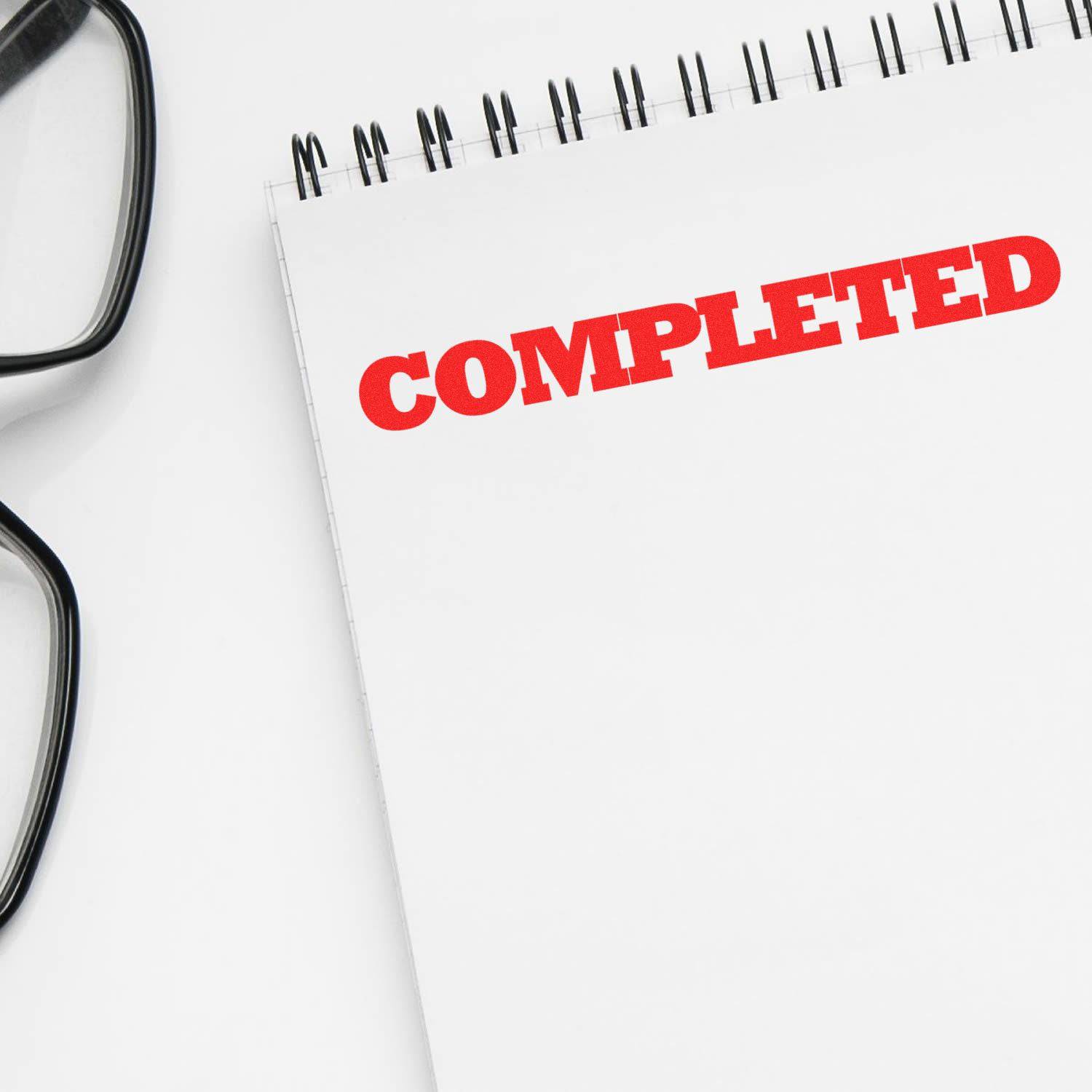 A notebook with COMPLETED stamped in red using the Large Self Inking Bold Completed Stamp, next to a pair of black glasses.