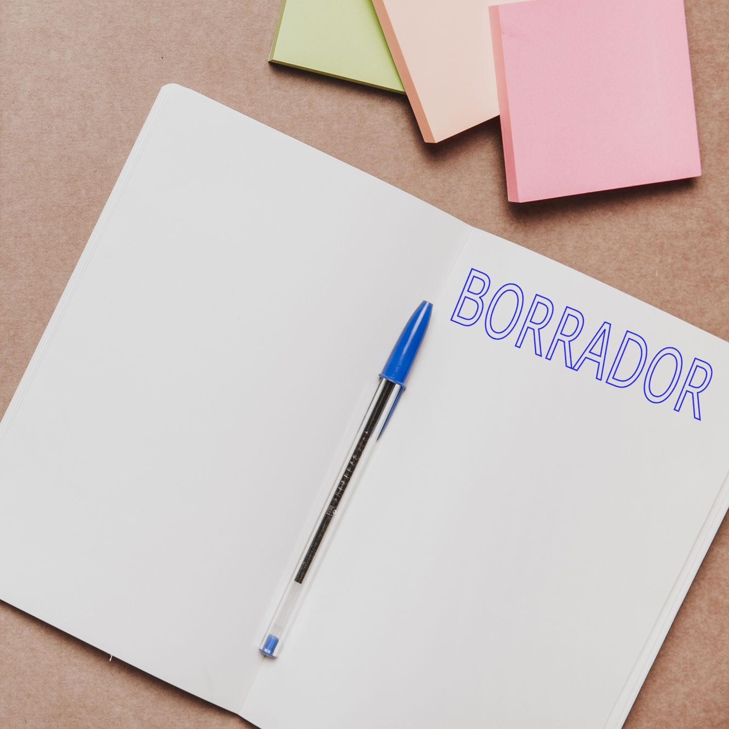 Open notebook with BORRADOR stamped in blue ink using the Large Borrador Rubber Stamp, surrounded by colorful sticky notes and a blue pen.