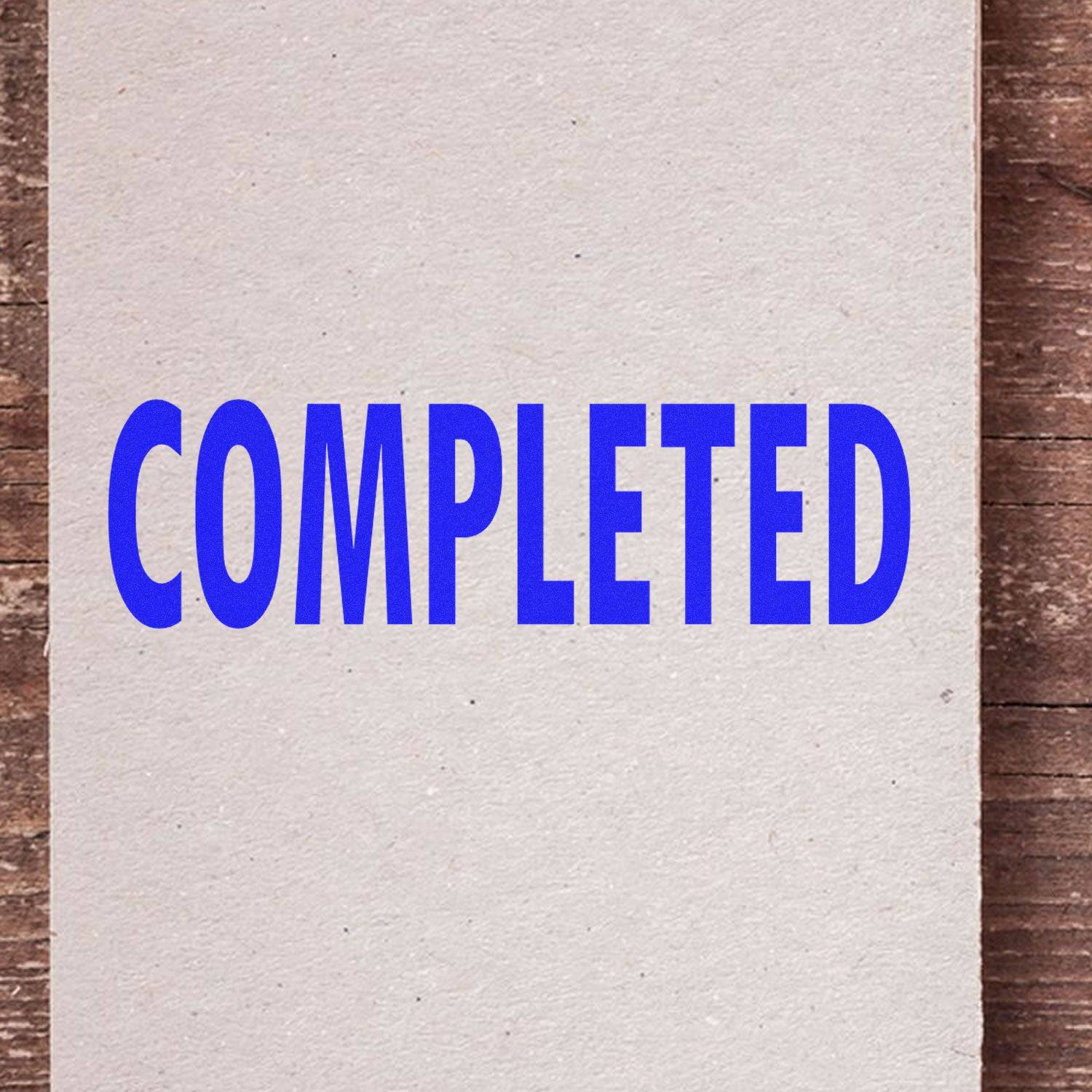 A piece of paper stamped with the word COMPLETED in bold blue letters using the Large Self Inking Completed Stamp, placed on a wooden surface.