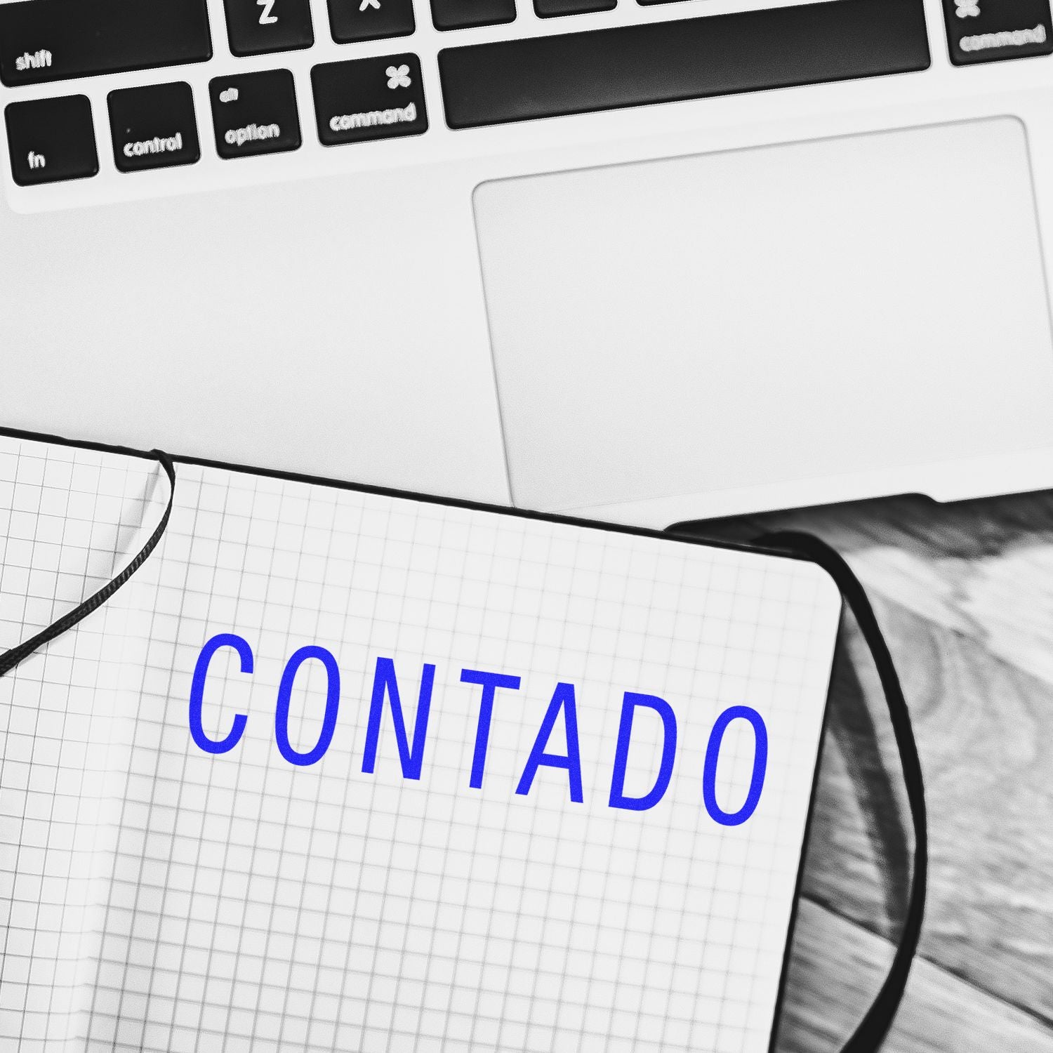 Slim Pre-Inked Contado Stamp used on a notebook, placed next to a laptop on a wooden desk.