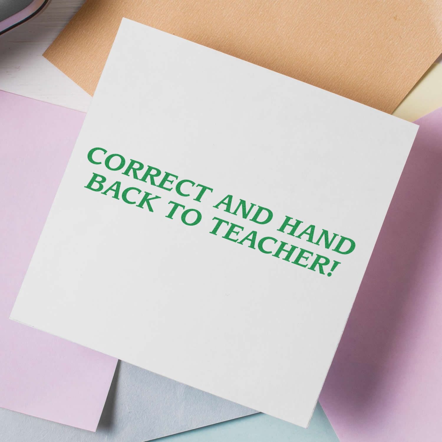 Self Inking Correct And Hand Back Teacher Stamp in use, showing the green text CORRECT AND HAND BACK TO TEACHER! on a white paper.