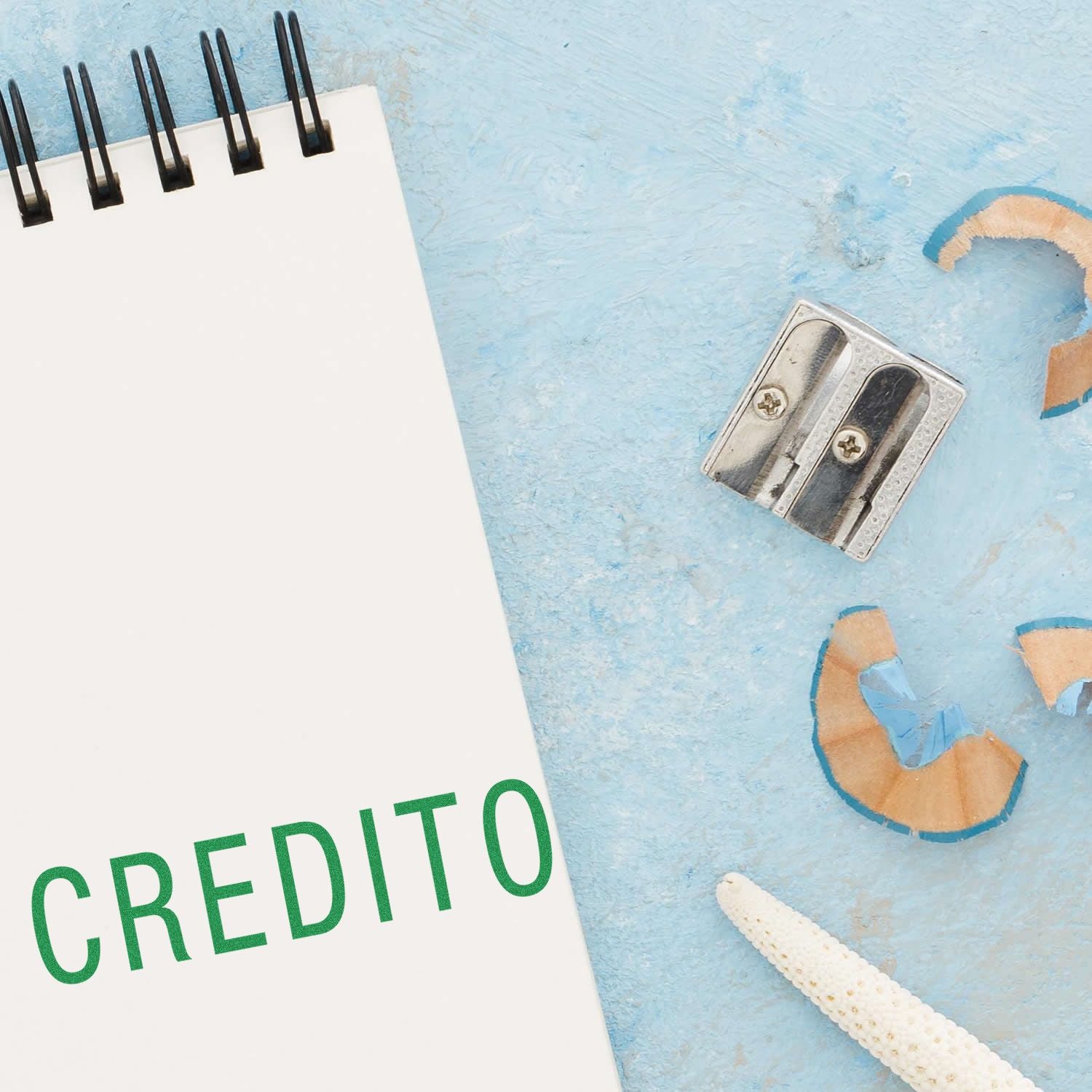 Credito Rubber Stamp on a notepad with a pencil sharpener and shavings on a light blue surface.