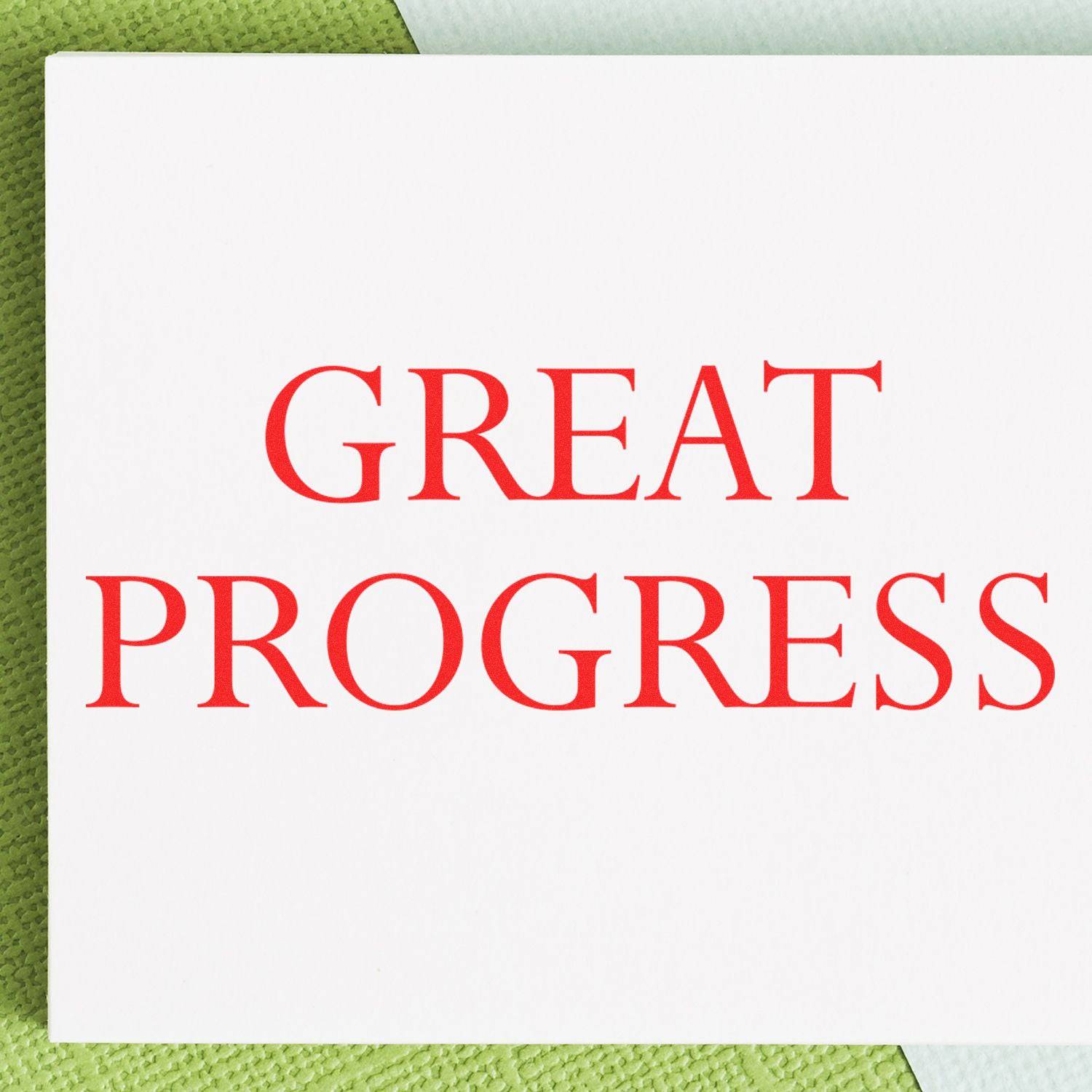 A white card stamped with GREAT PROGRESS in red ink using the Large Pre-Inked Great Progress Stamp, placed on a green textured surface.