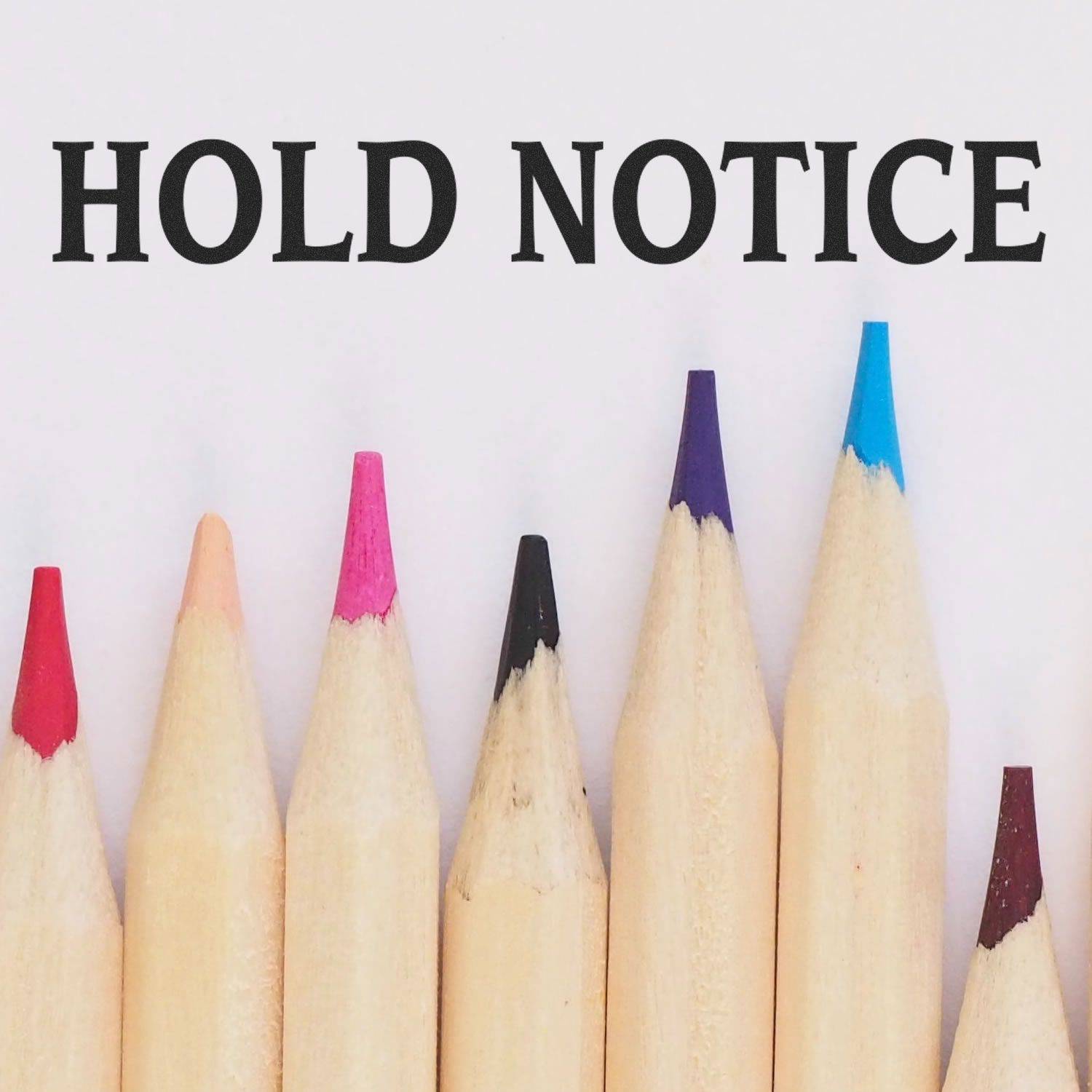 Large Pre-Inked Hold Notice Stamp in use, with the words HOLD NOTICE stamped above a row of colorful pencil tips.