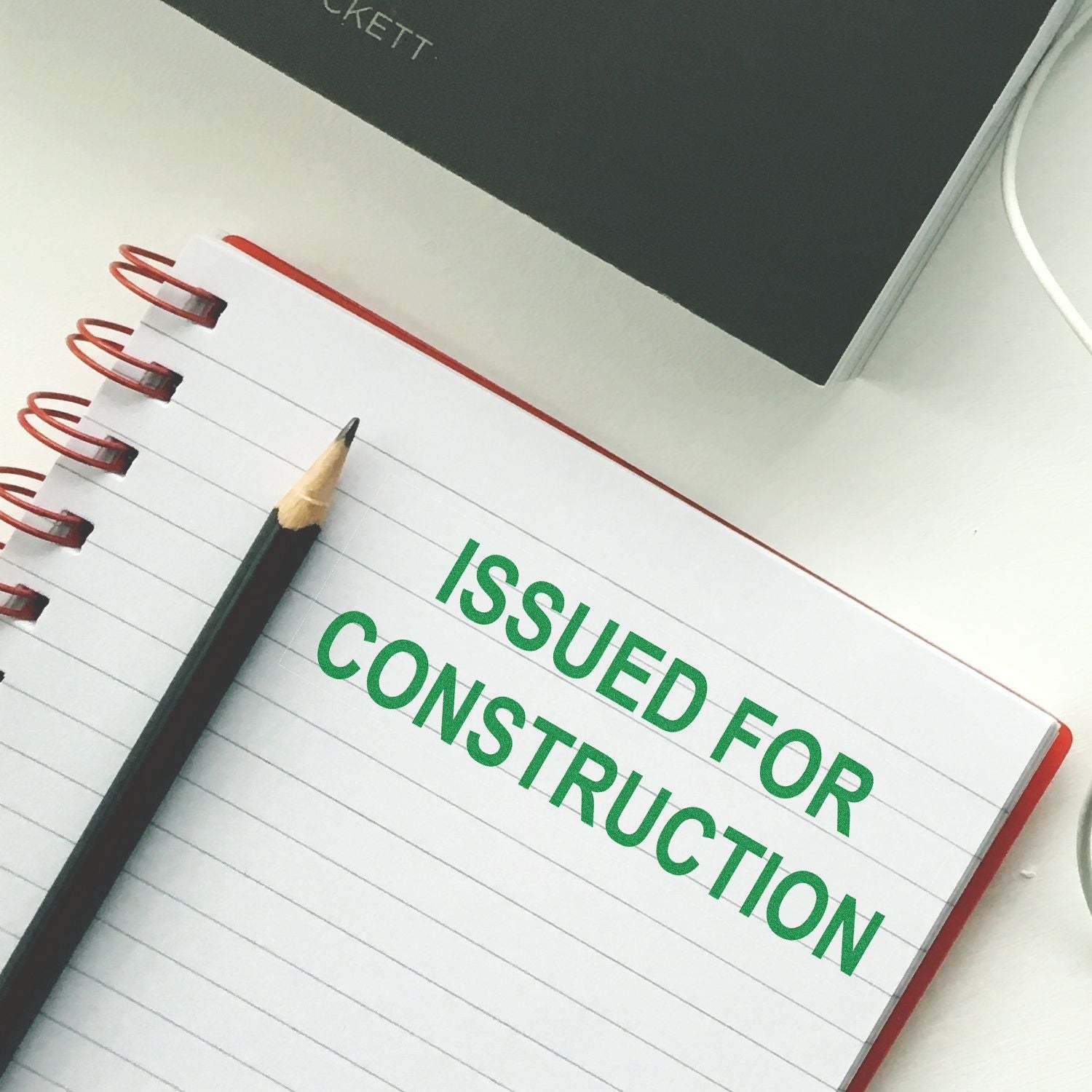 Self Inking Issued for Construction Stamp in green ink on a spiral notebook with a pencil beside it.