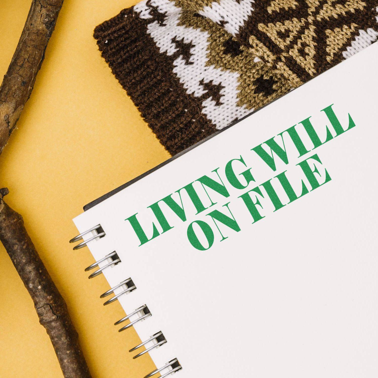 Large Pre-Inked Living Will On File Stamp used on a spiral notebook, with a knitted item and wooden sticks in the background.