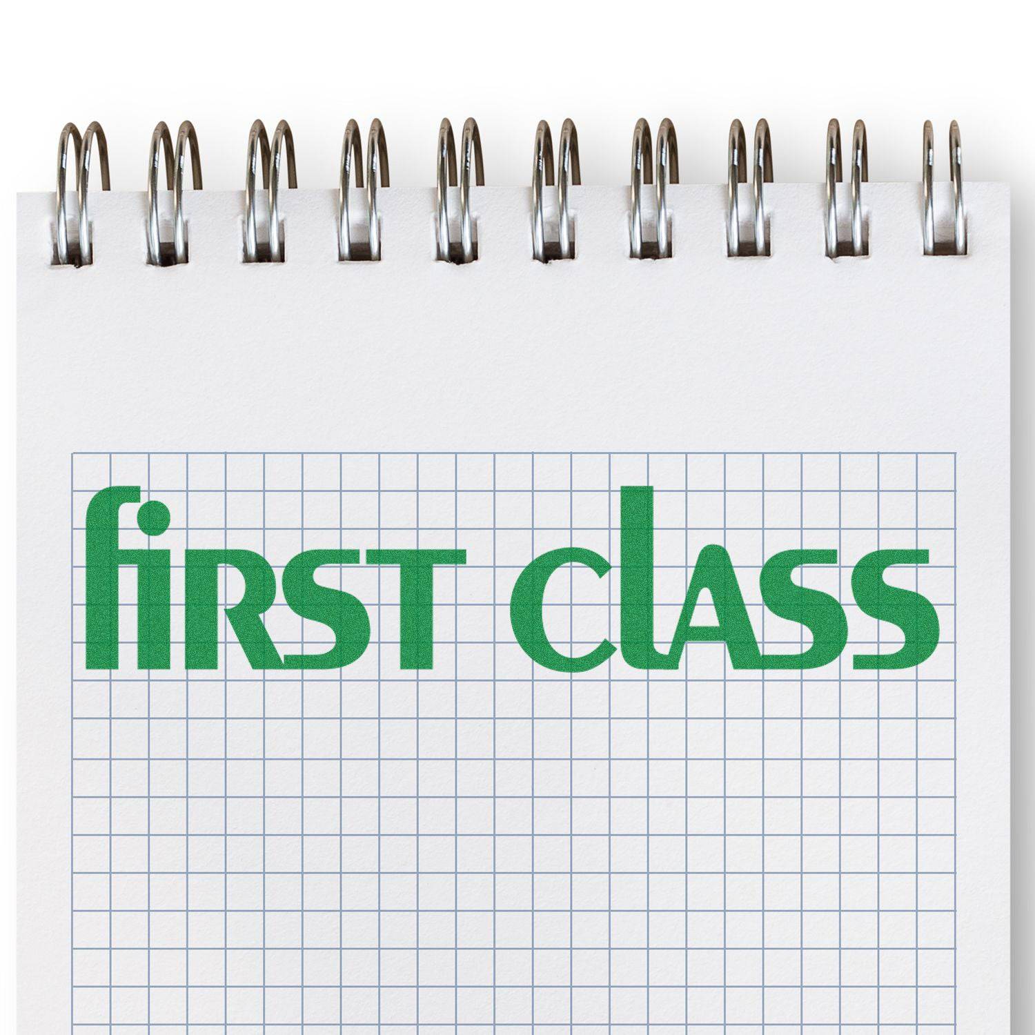 Large Pre-Inked Lower Case First Class Stamp in green ink on a spiral-bound graph paper notebook.