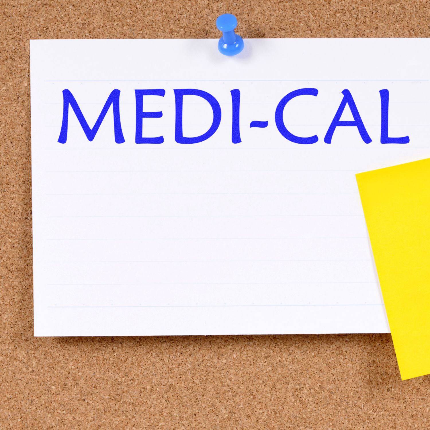 A corkboard with a white card stamped MEDI-CAL using the Large Pre-Inked Medi-Cal Stamp, pinned with a blue pushpin and a yellow sticky note.