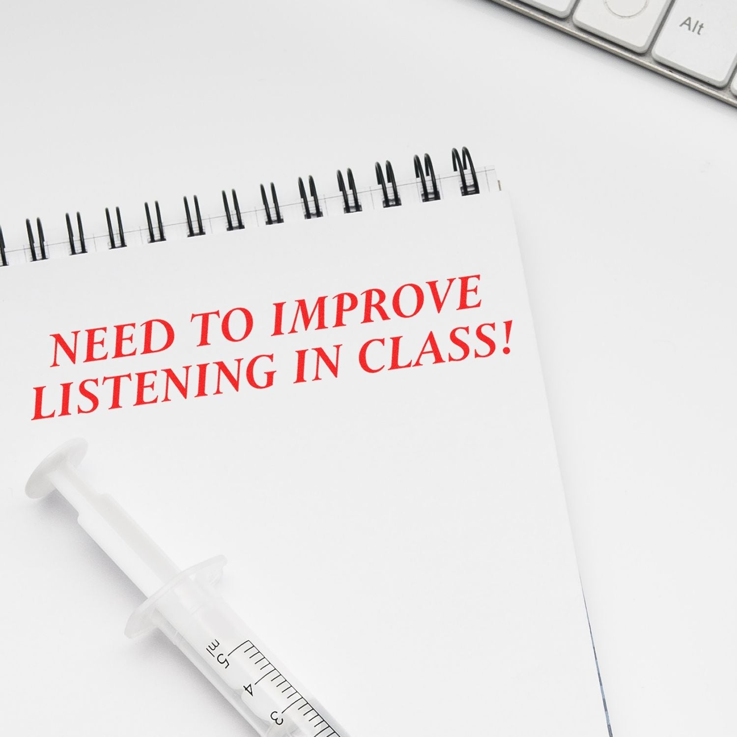 Self Inking Need To Improve Listening Stamp used on a notebook with red text NEED TO IMPROVE LISTENING IN CLASS! next to a keyboard and syringe pen.