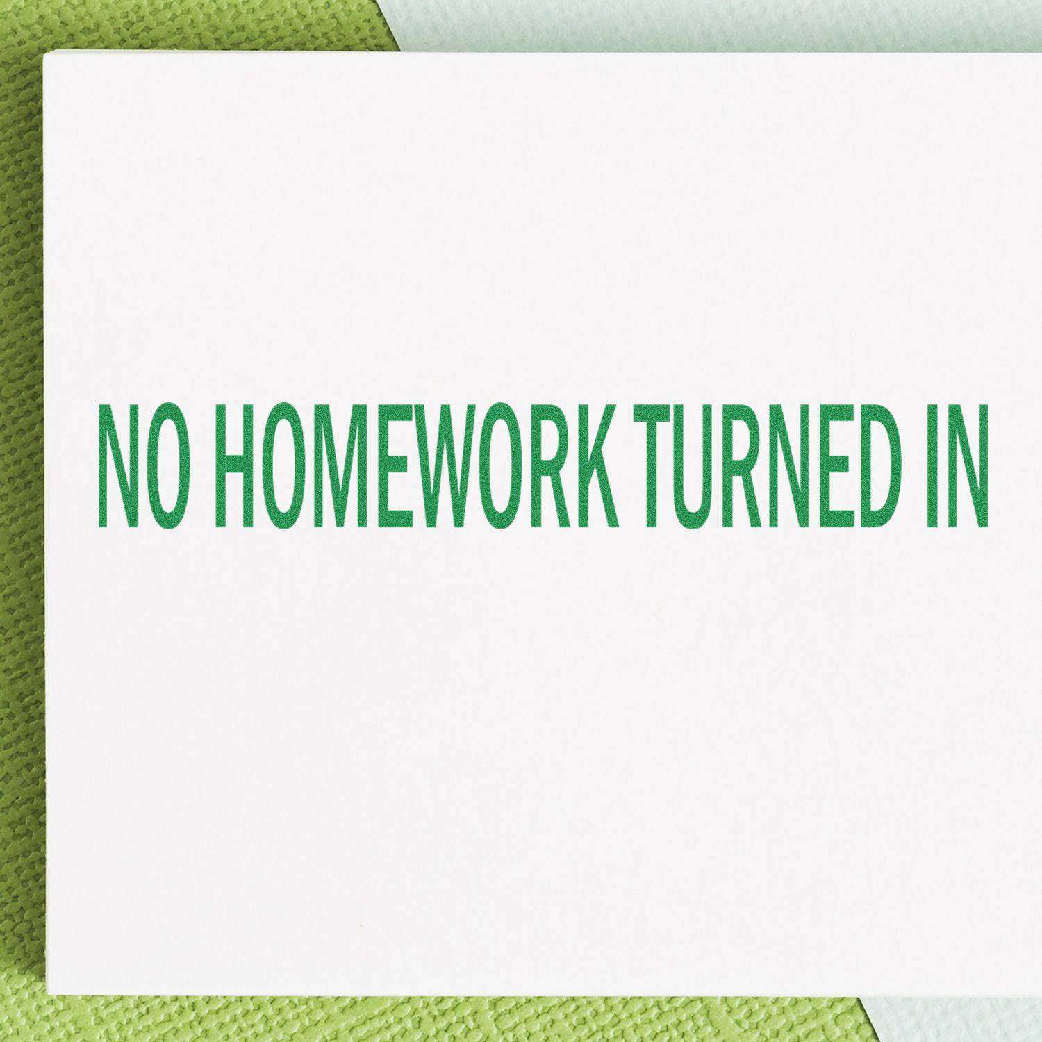 Large Pre-Inked No Homework Turned In Stamp in green ink on white paper, placed on a green textured surface.