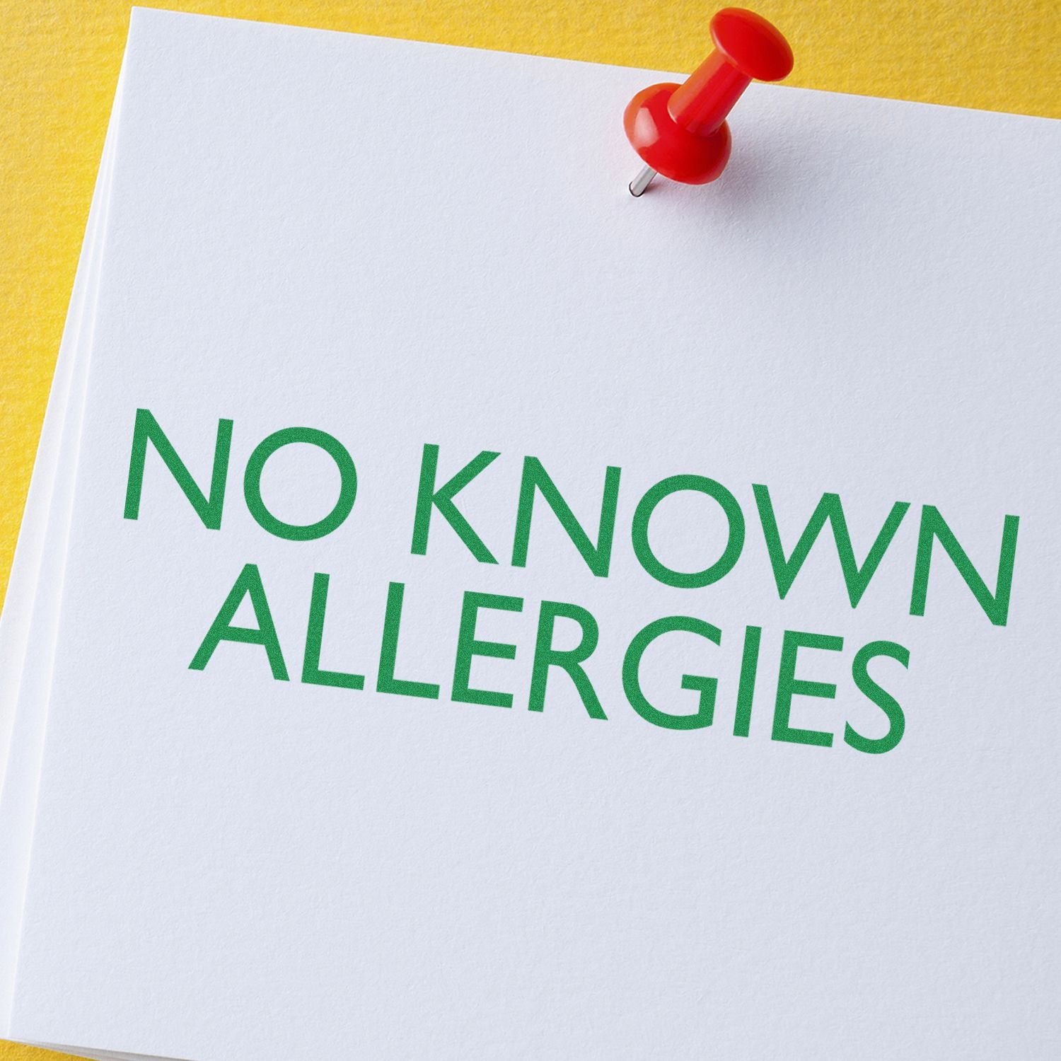 Large No Known Allergies Rubber Stamp used on white paper with green text, pinned with a red pushpin on a yellow background.