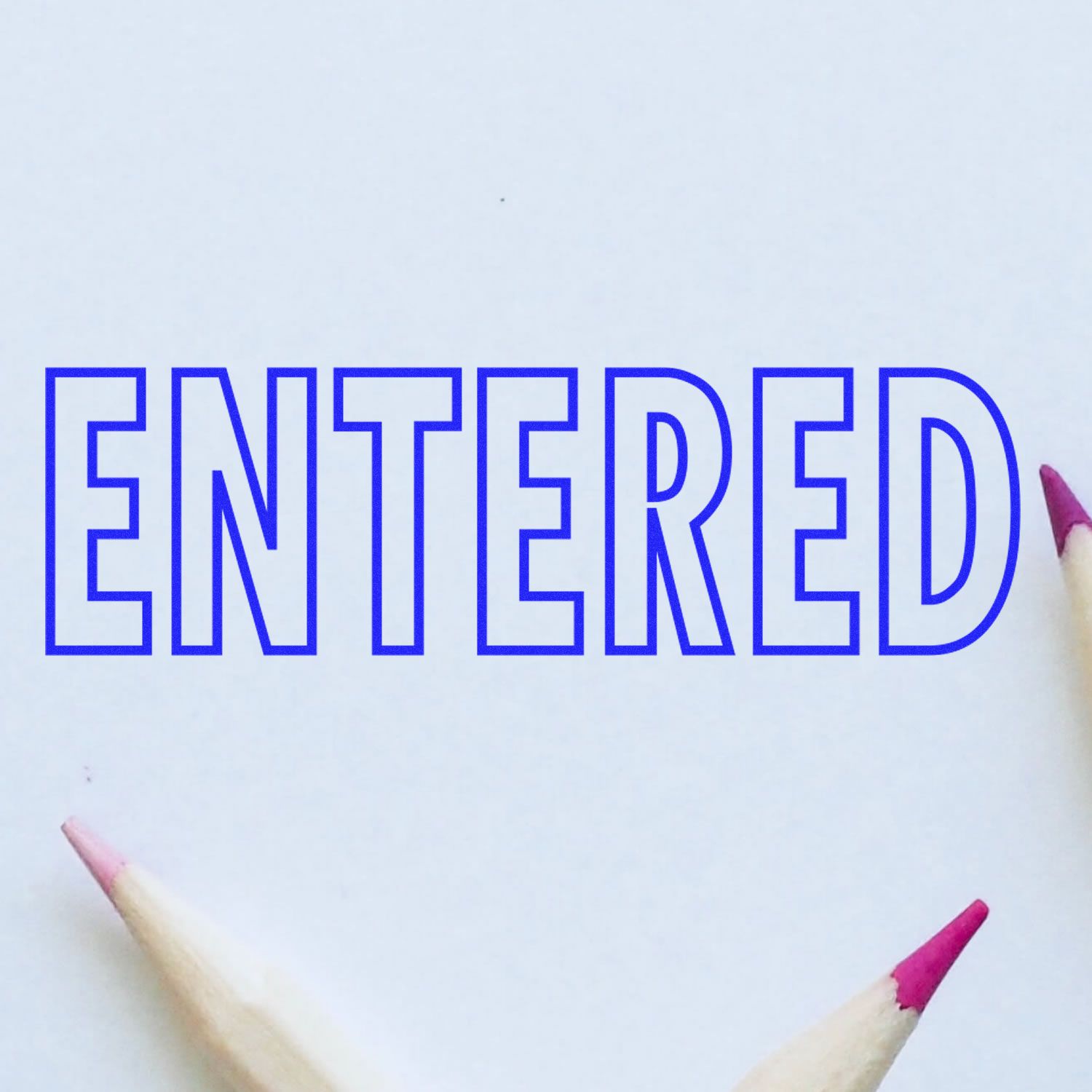 Large Self Inking Entered Stamp Outline Text in blue ink on white paper, surrounded by pencils with pink tips.