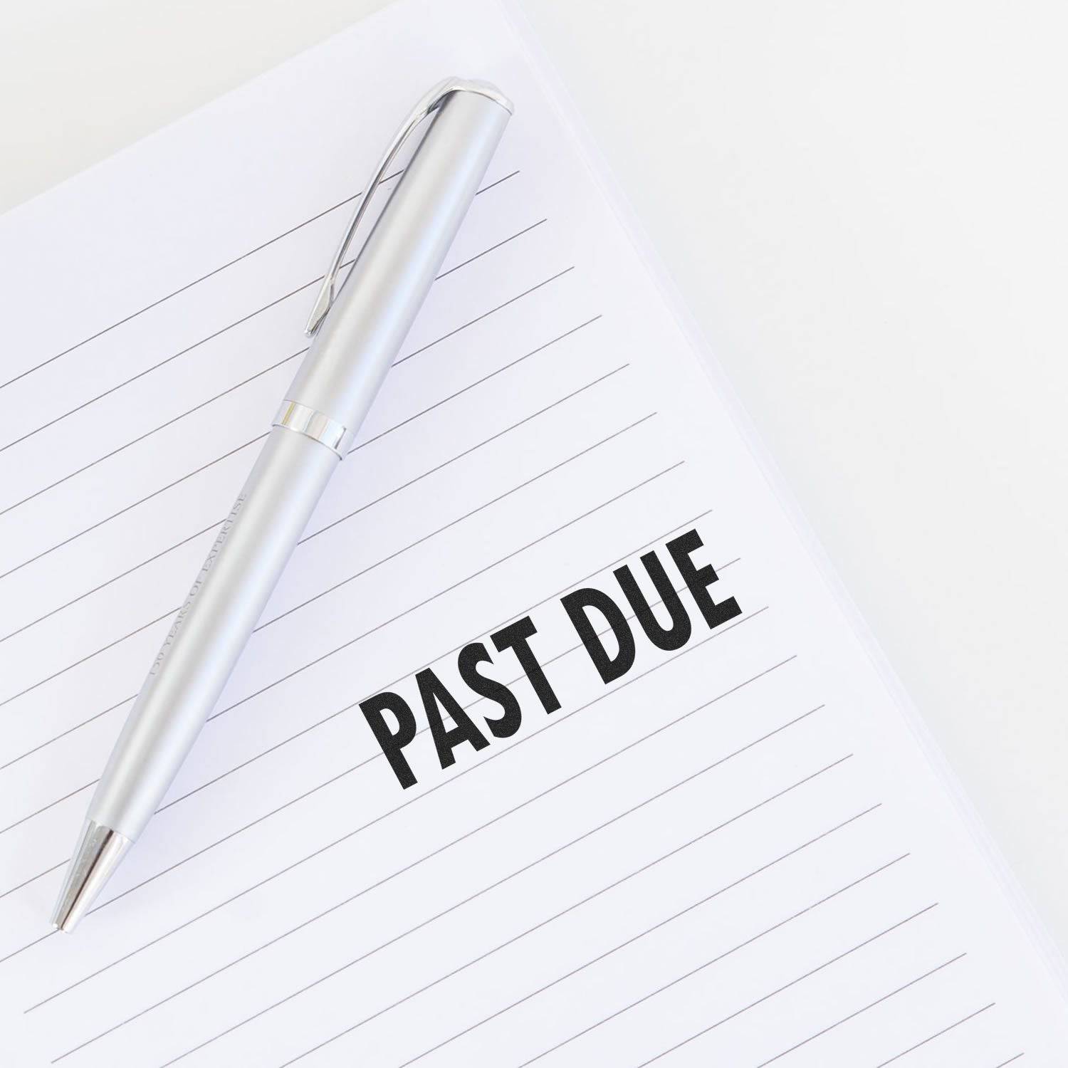 A silver pen lies on a lined paper with PAST DUE stamped in bold black letters using the Large Past Due Rubber Stamp.