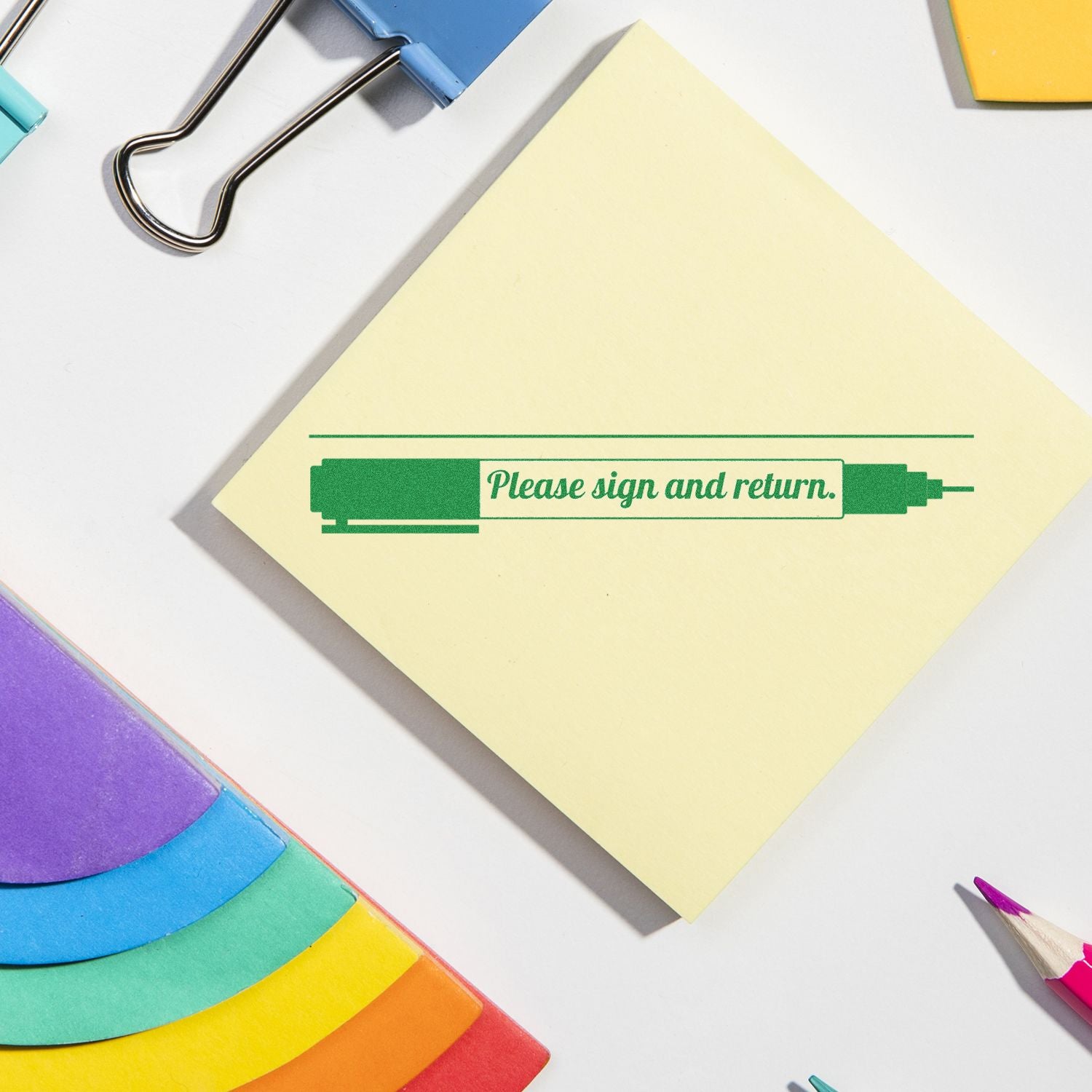 Please Sign and Return with Pen Rubber Stamp on a yellow sticky note surrounded by colorful office supplies.