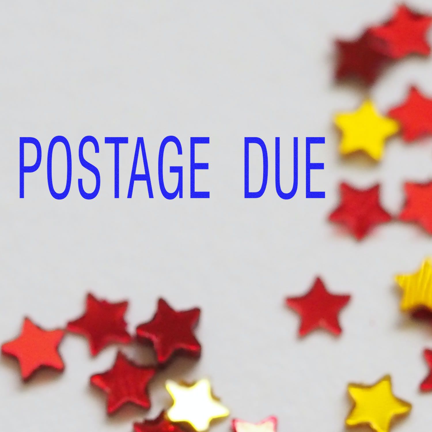 Large Self Inking Postage Due Stamp in blue ink on white paper, surrounded by red and yellow star-shaped confetti.