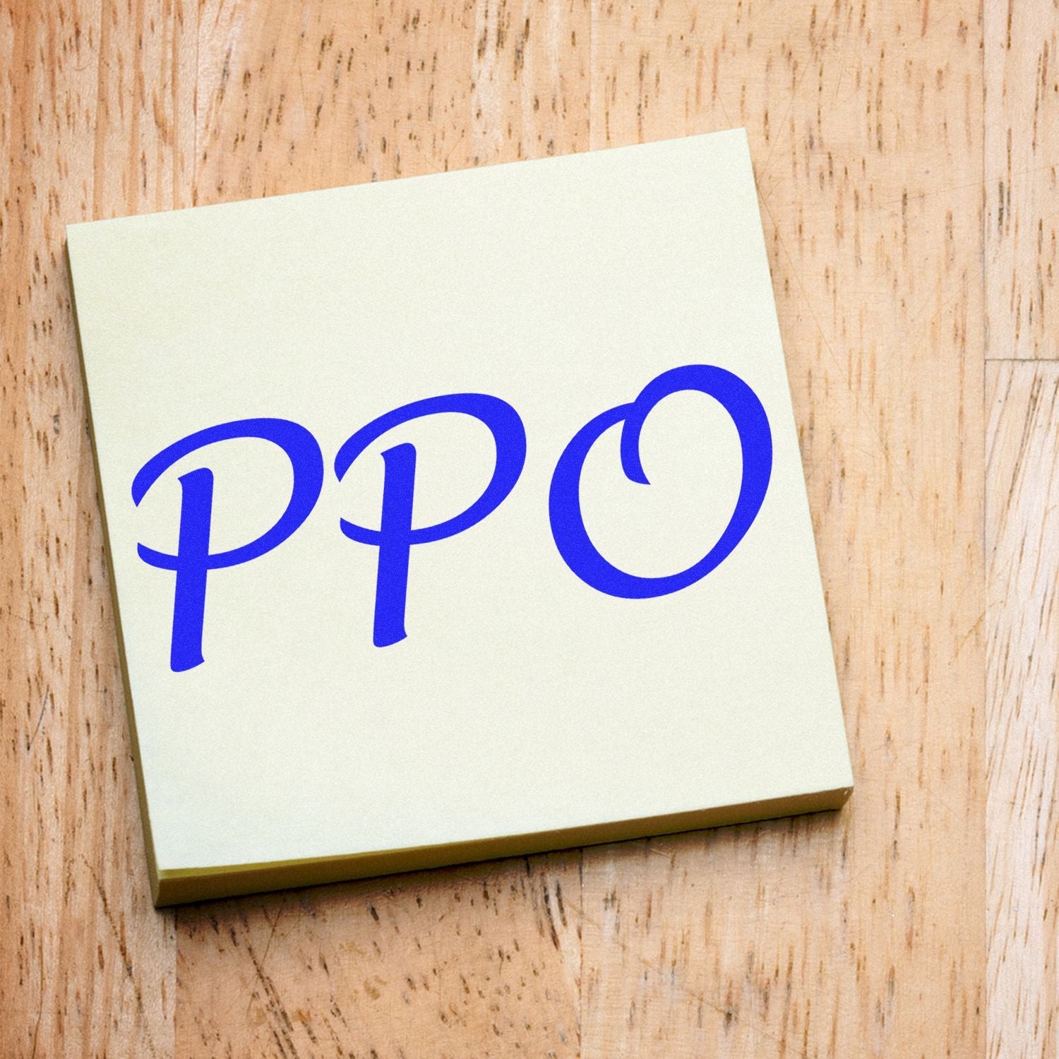Self Inking PPO Stamp in use, displaying the blue PPO imprint on a light-colored sticky note on a wooden surface.