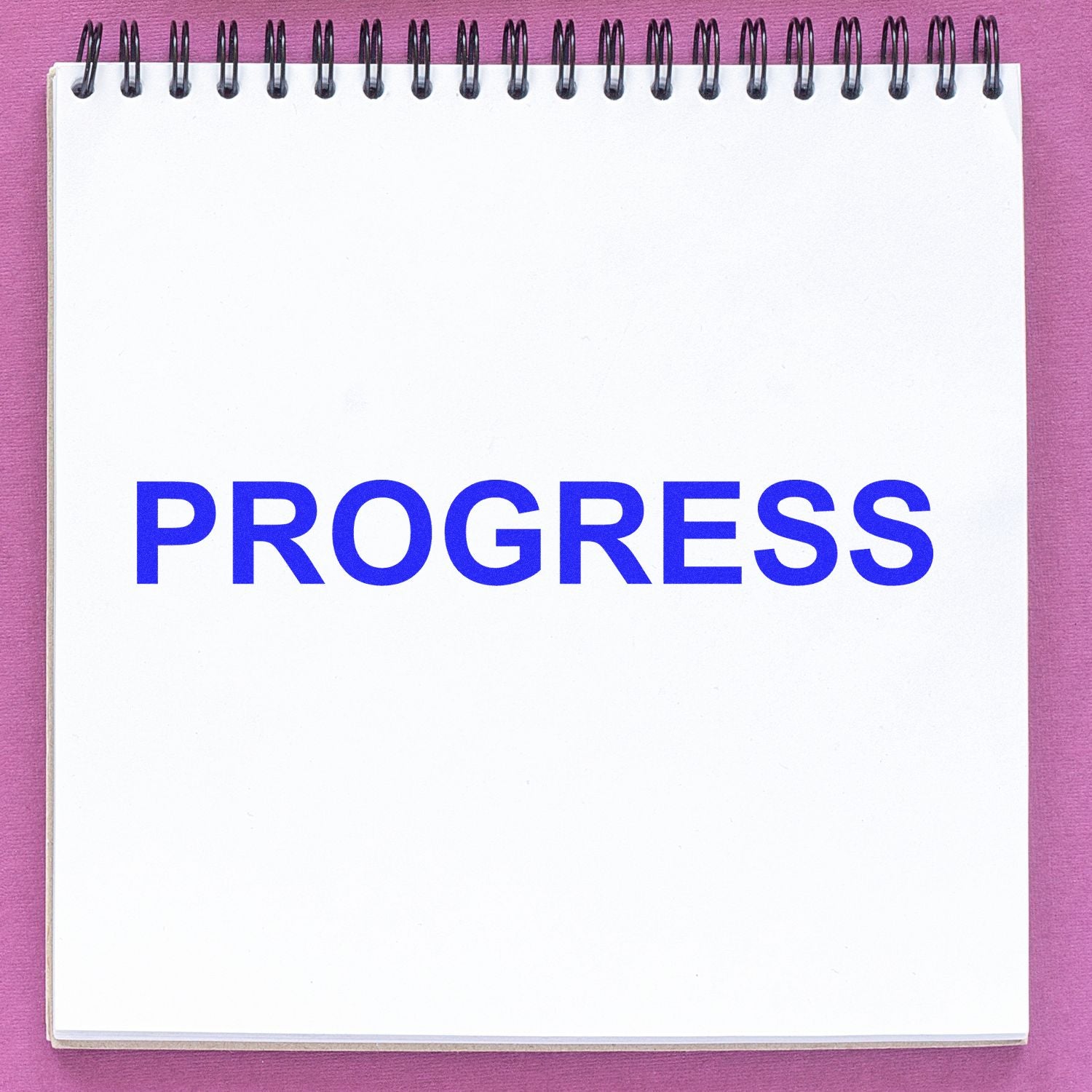 A notebook with the word PROGRESS stamped in blue ink using a Slim Pre-Inked Progress Stamp on a pink background.