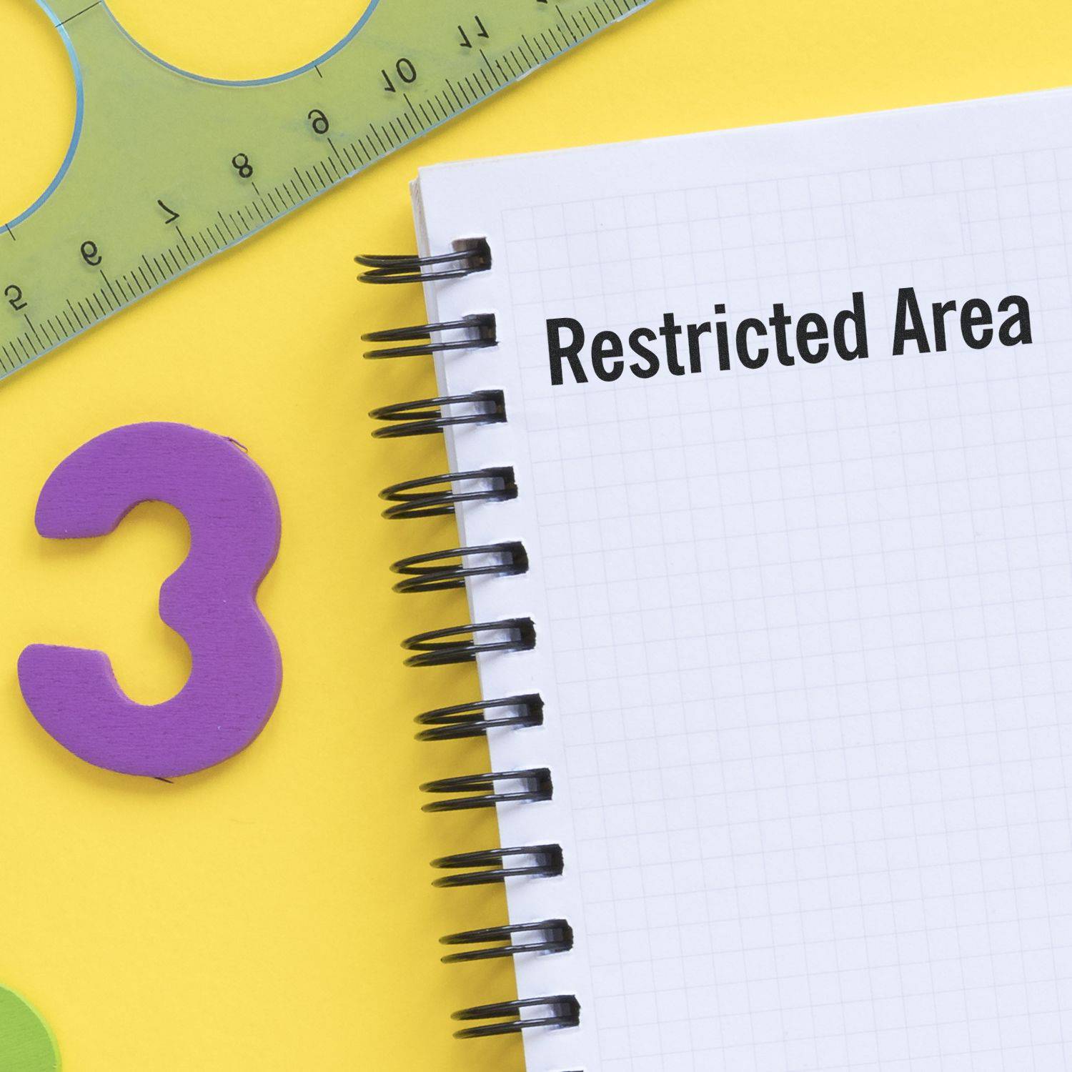 A notebook stamped with Restricted Area using the Large Pre-Inked Restricted Area Stamp, placed on a yellow surface with a ruler and a purple number 3.