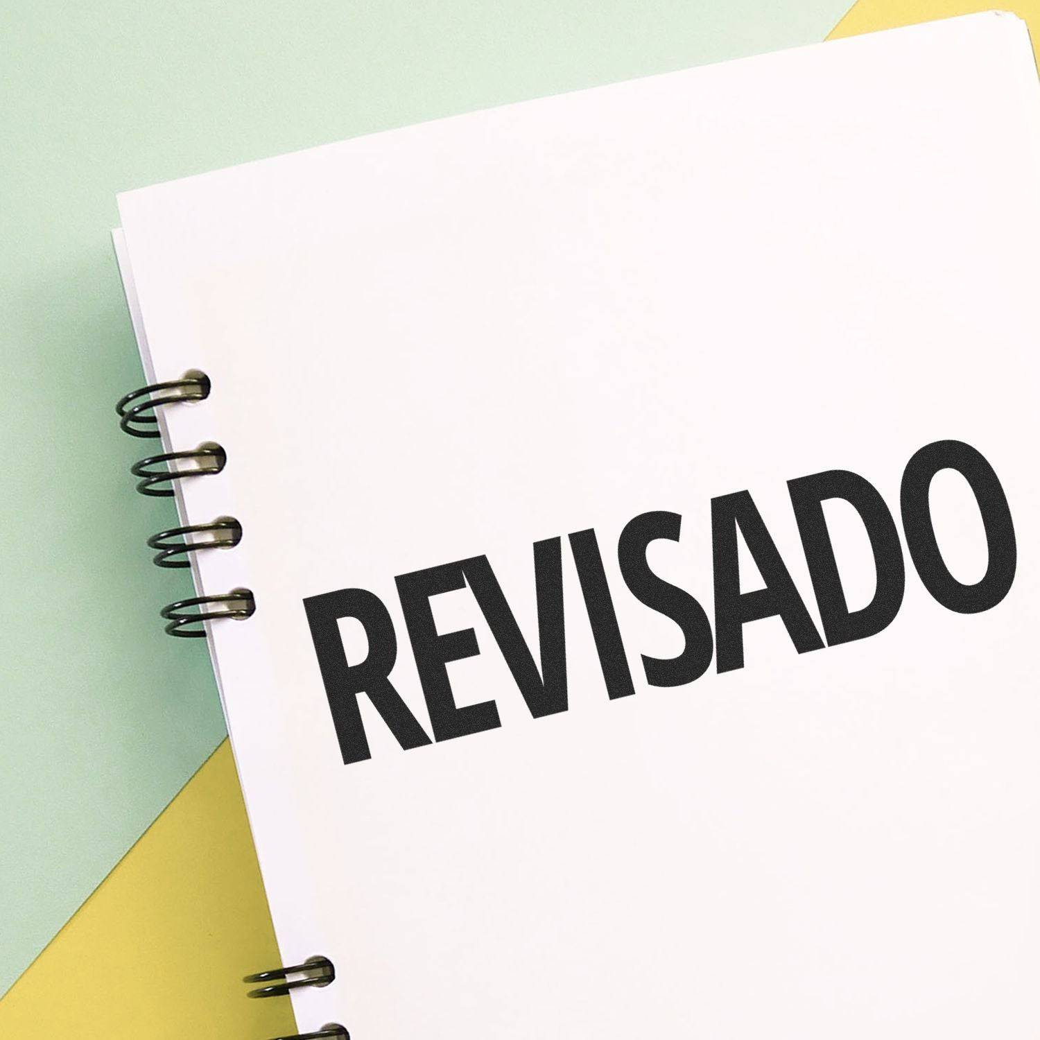 A notebook with REVISADO stamped on a page using the Large Pre-Inked Revisado Stamp, placed on a pastel-colored background.