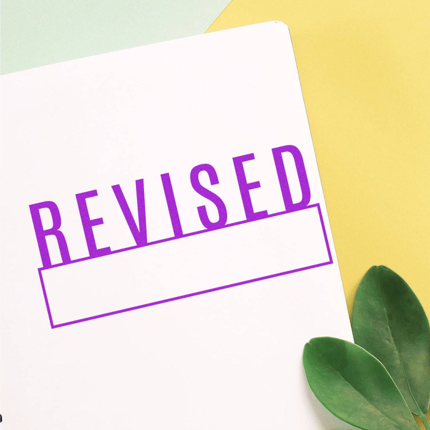 Large Revised with Box Rubber Stamp in purple ink on white paper, with green leaves and yellow background.