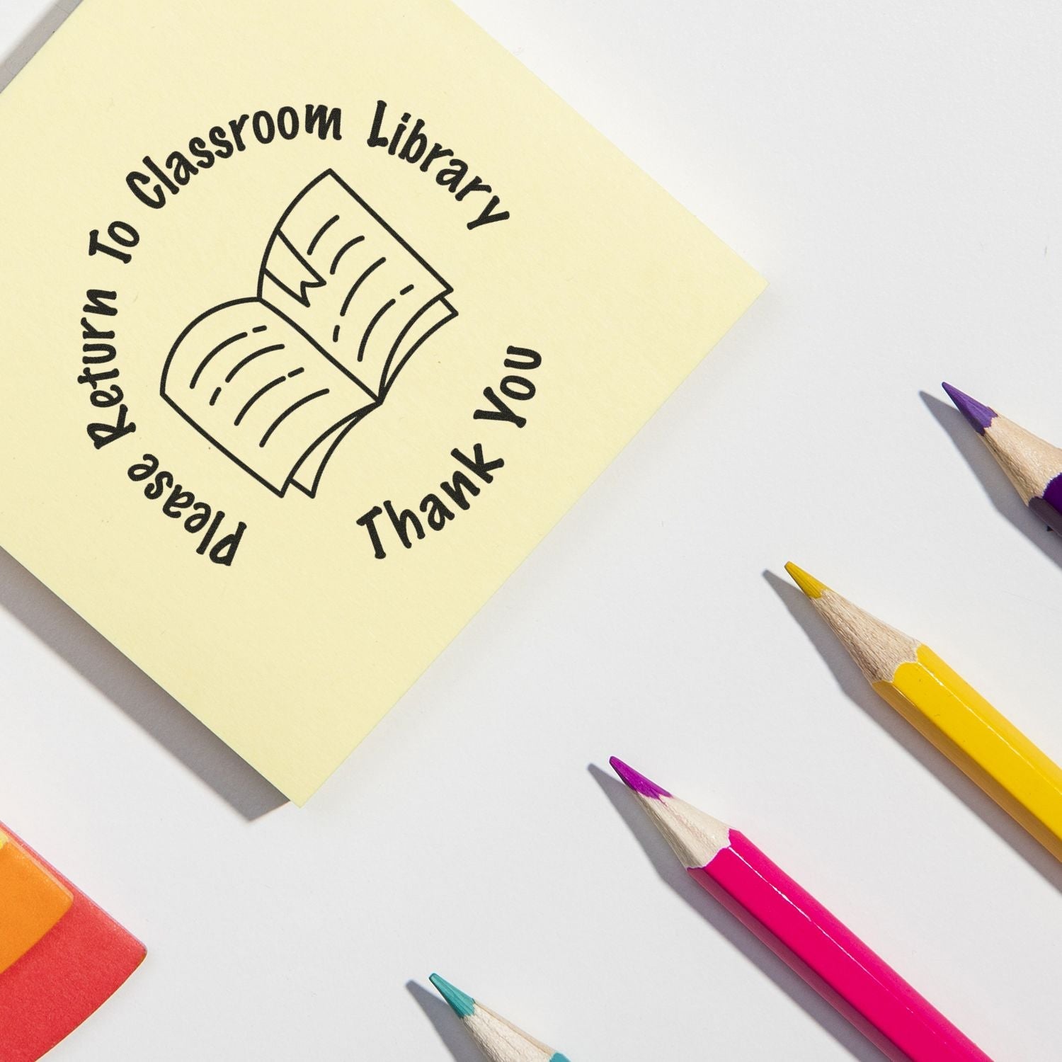 Sticky note stamped with Please Return to Classroom Library using the Self Inking Round Please Return to Classroom Library Stamp, surrounded by pencils.