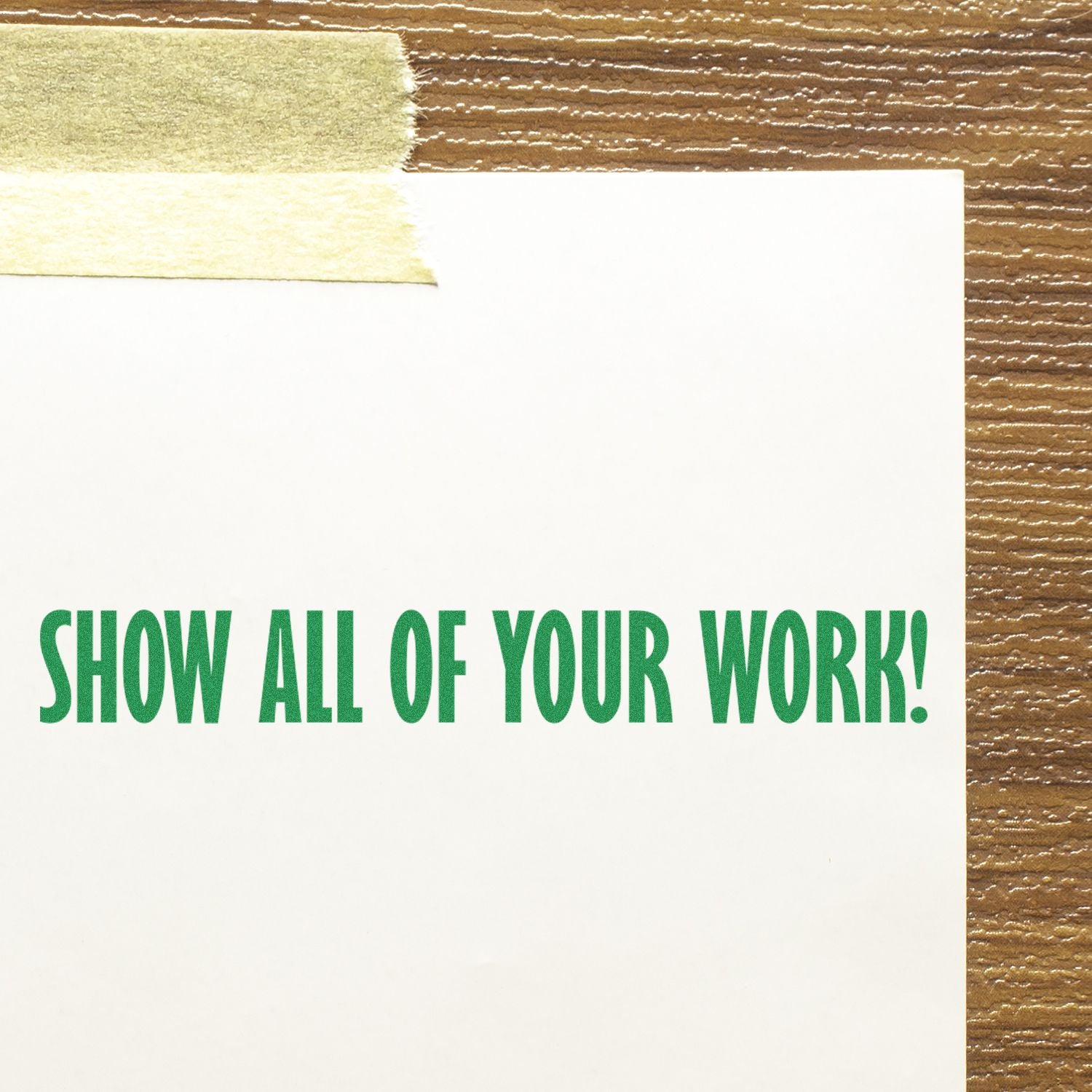 Large Show All Of Your Work rubber stamp in green ink on white paper, taped to a wooden surface.