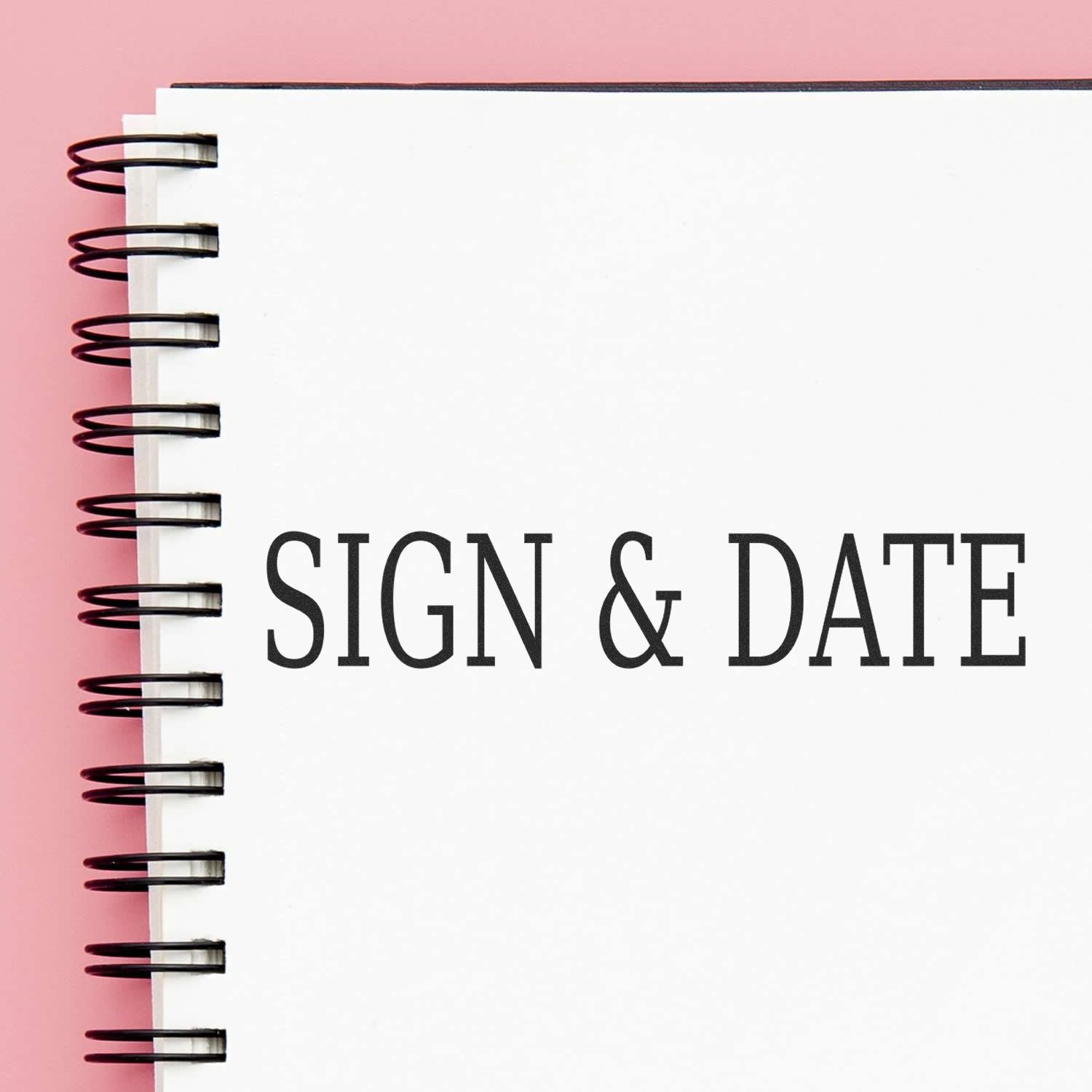 Large Sign & Date Rubber Stamp used on a spiral-bound notebook with a pink background.