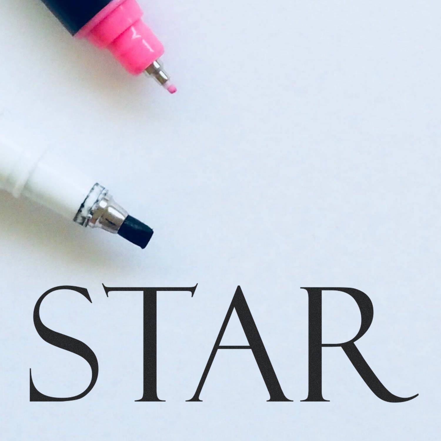 Two markers and the Large Pre-Inked Star Stamp on white paper with the word STAR stamped in black.