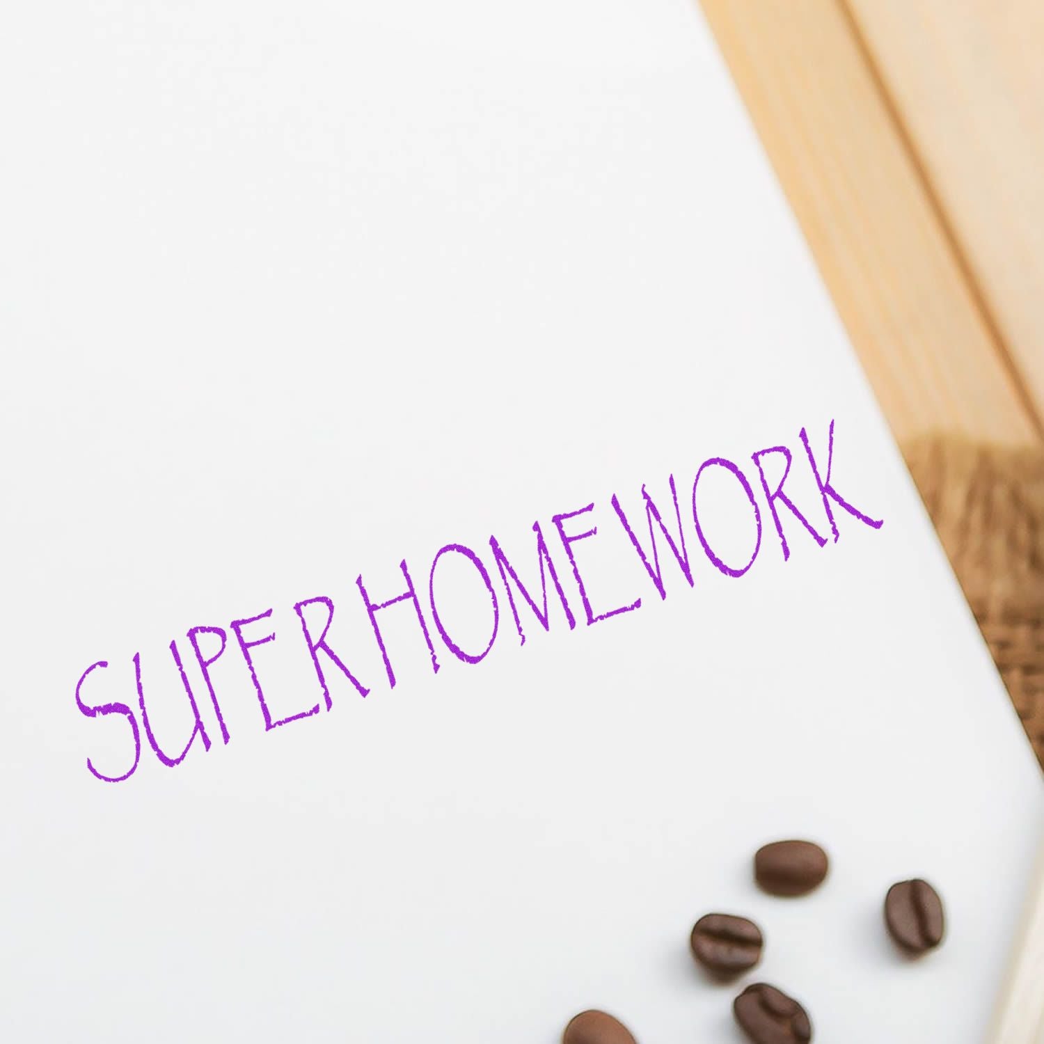 Large Super Homework Rubber Stamp in purple ink on white paper, with coffee beans scattered nearby on a wooden surface.