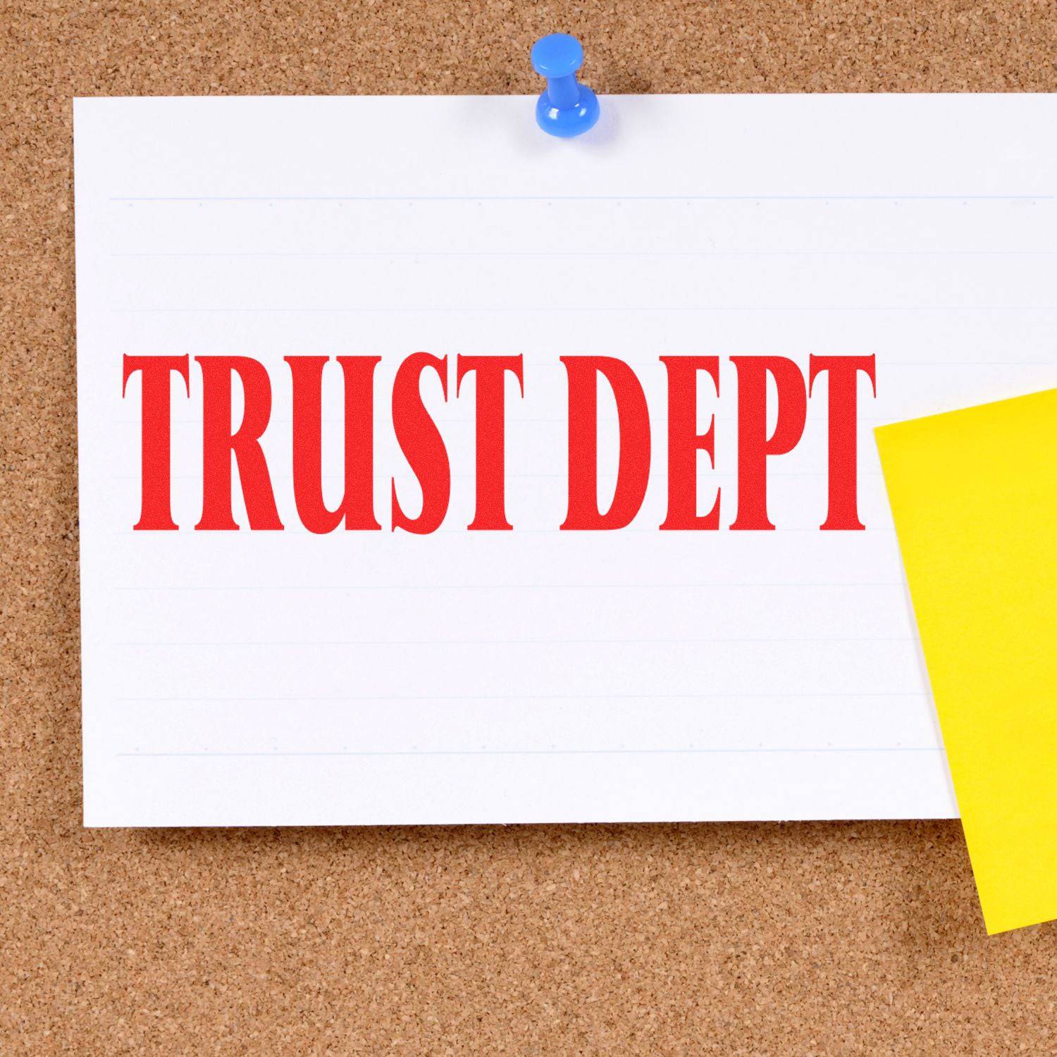 A Large Pre-Inked Trust Dept Stamp imprint on a white card pinned to a corkboard, with a yellow sticky note beside it.