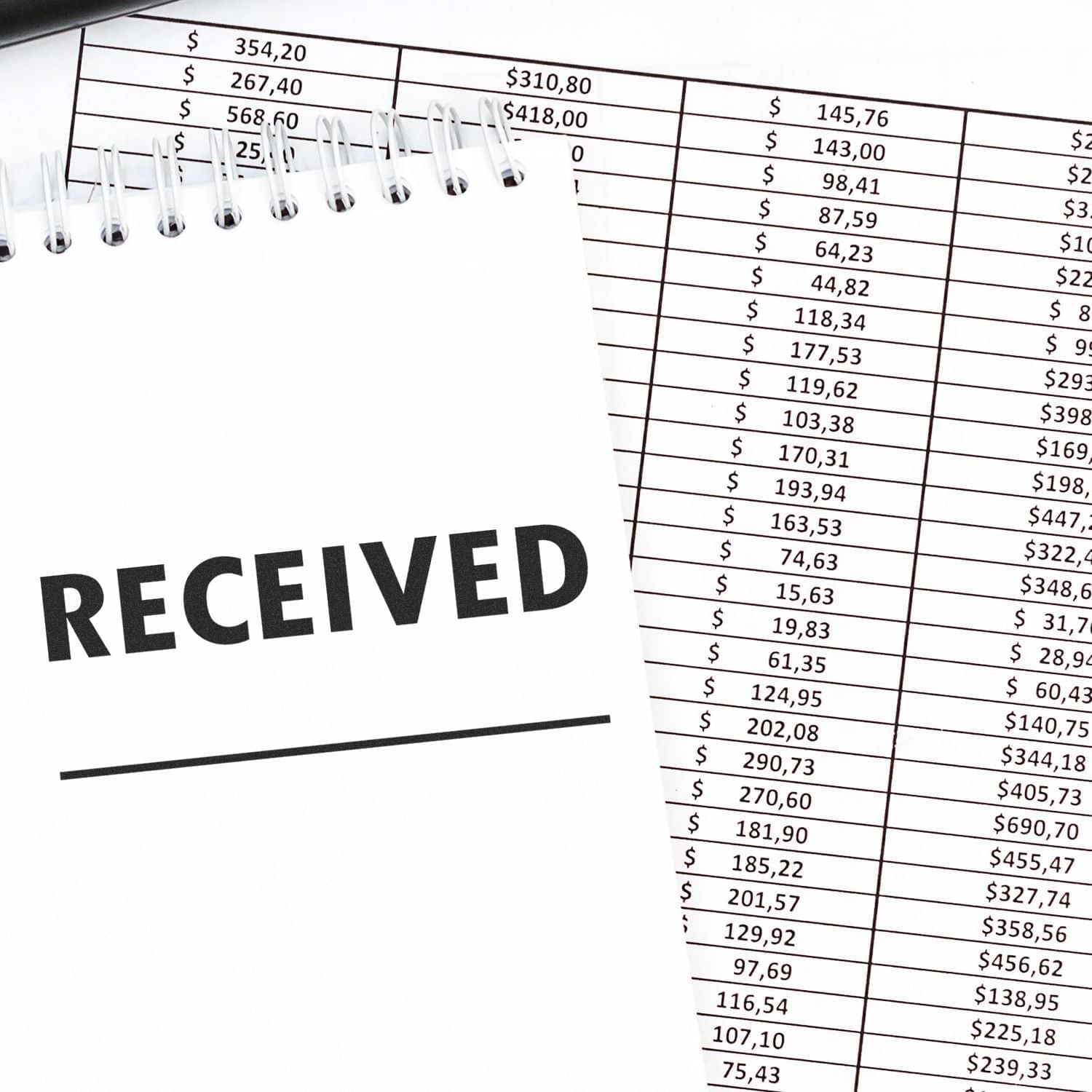 Large Pre-Inked Two Line Received Stamp used on a notepad, placed on top of financial documents with various amounts listed.