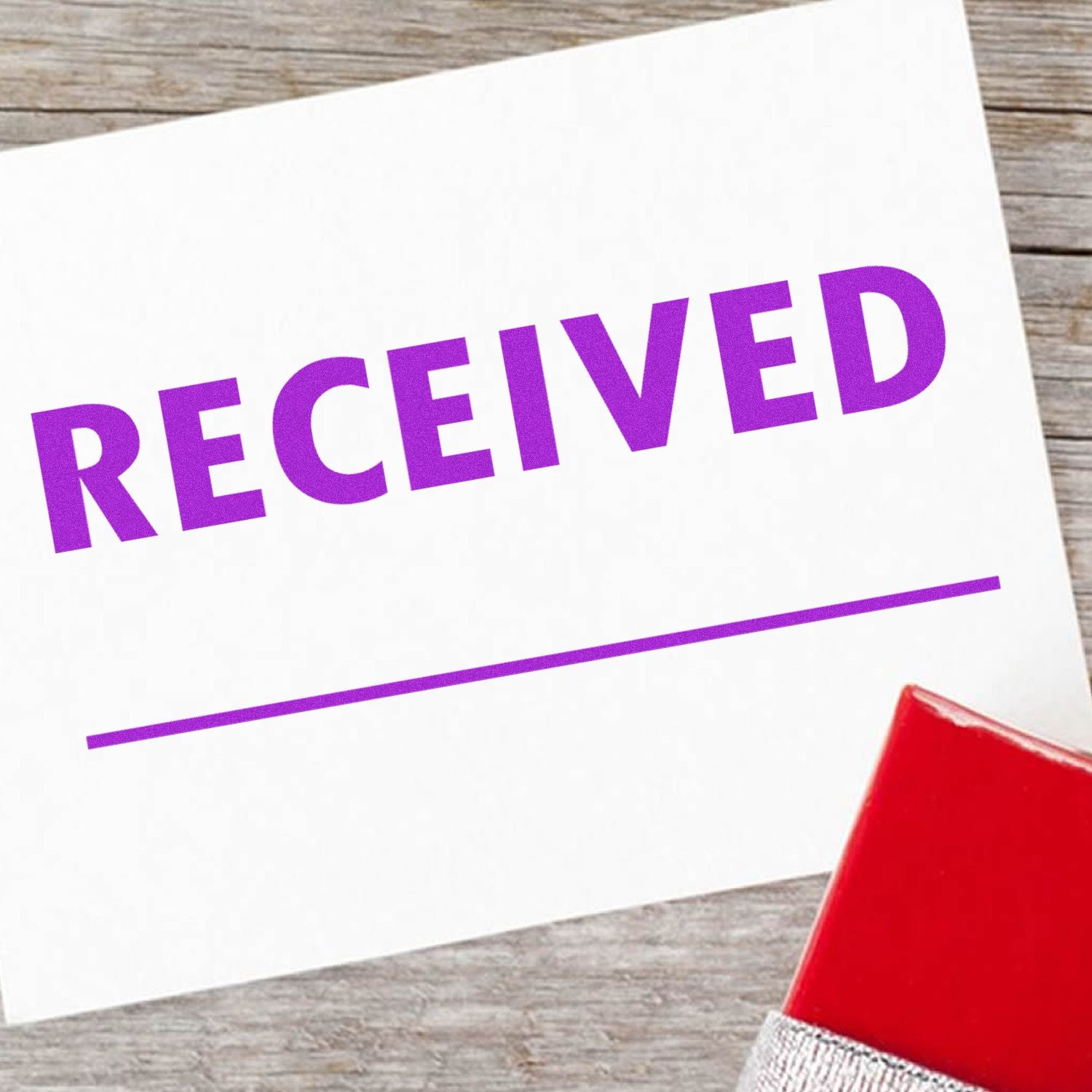 Large Two Line Received Rubber Stamp in purple ink on white paper, with a red stamp handle visible on a wooden surface.