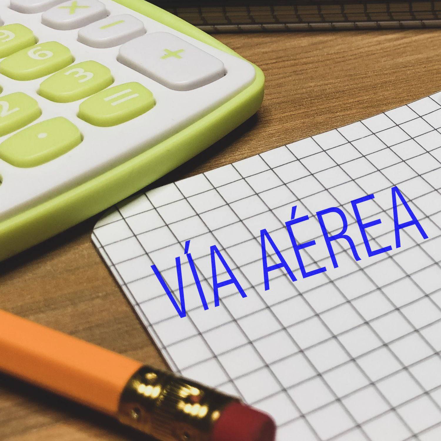 Large Pre-Inked Via Aerea Stamp used on graph paper next to a pencil, calculator, and notebook on a wooden desk.