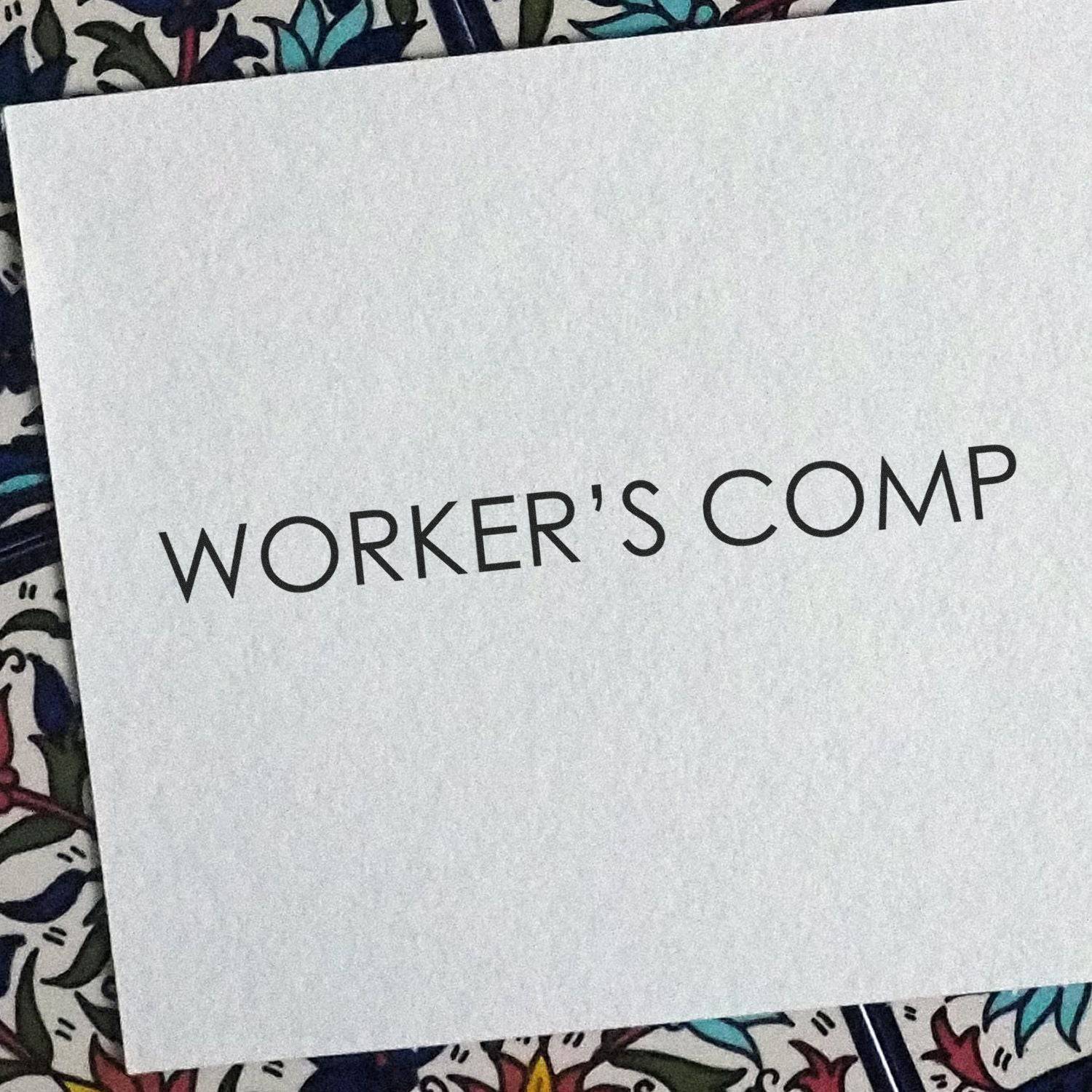 A document stamped with WORKER'S COMP using the Large Pre-Inked Workers Comp Stamp, placed on a patterned surface.