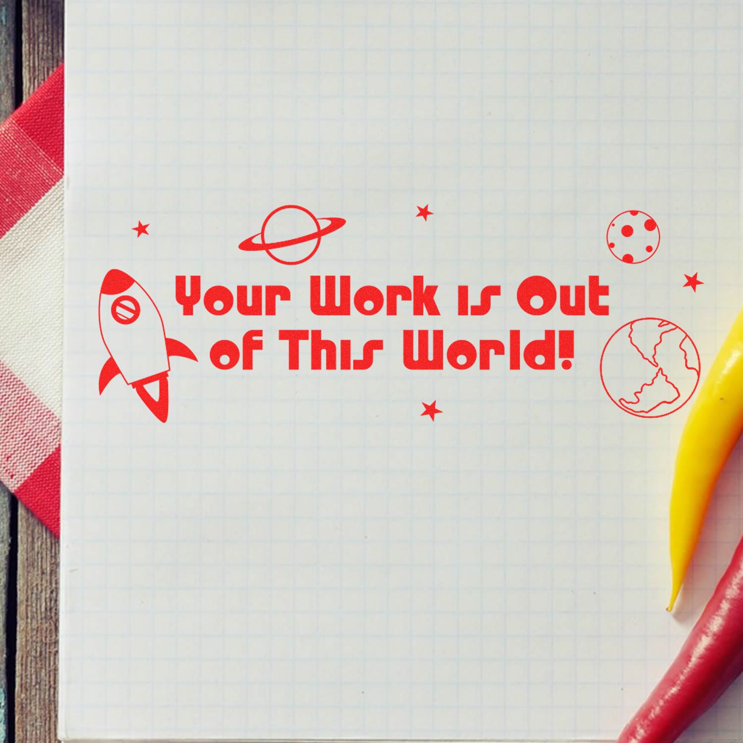 Large Your Work is Out of This World rubber stamp in red ink on graph paper, with a rocket, planet, and stars design.
