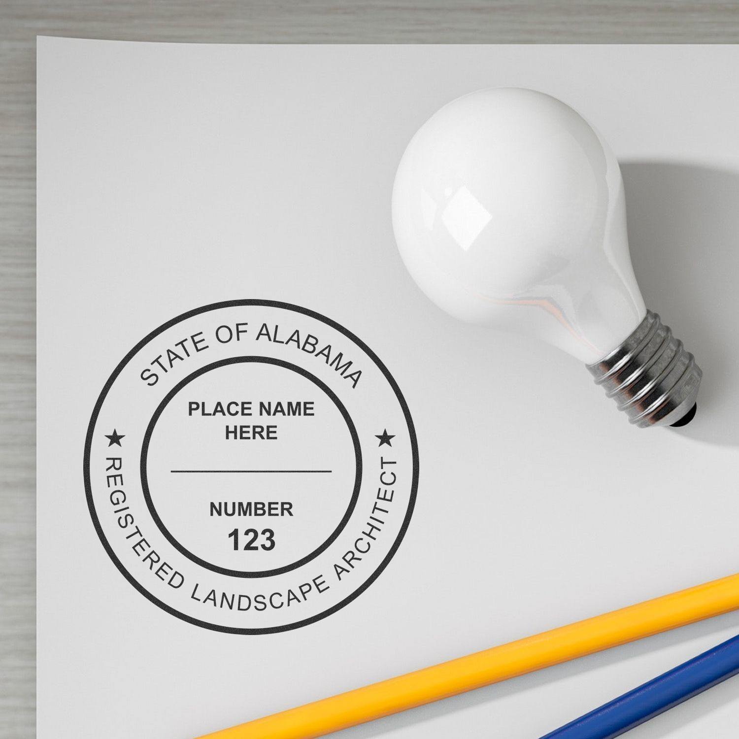 Xstamper Landscape Architect Pre-Inked Rubber Stamp of Seal in use on a white paper with a light bulb and pencils nearby.