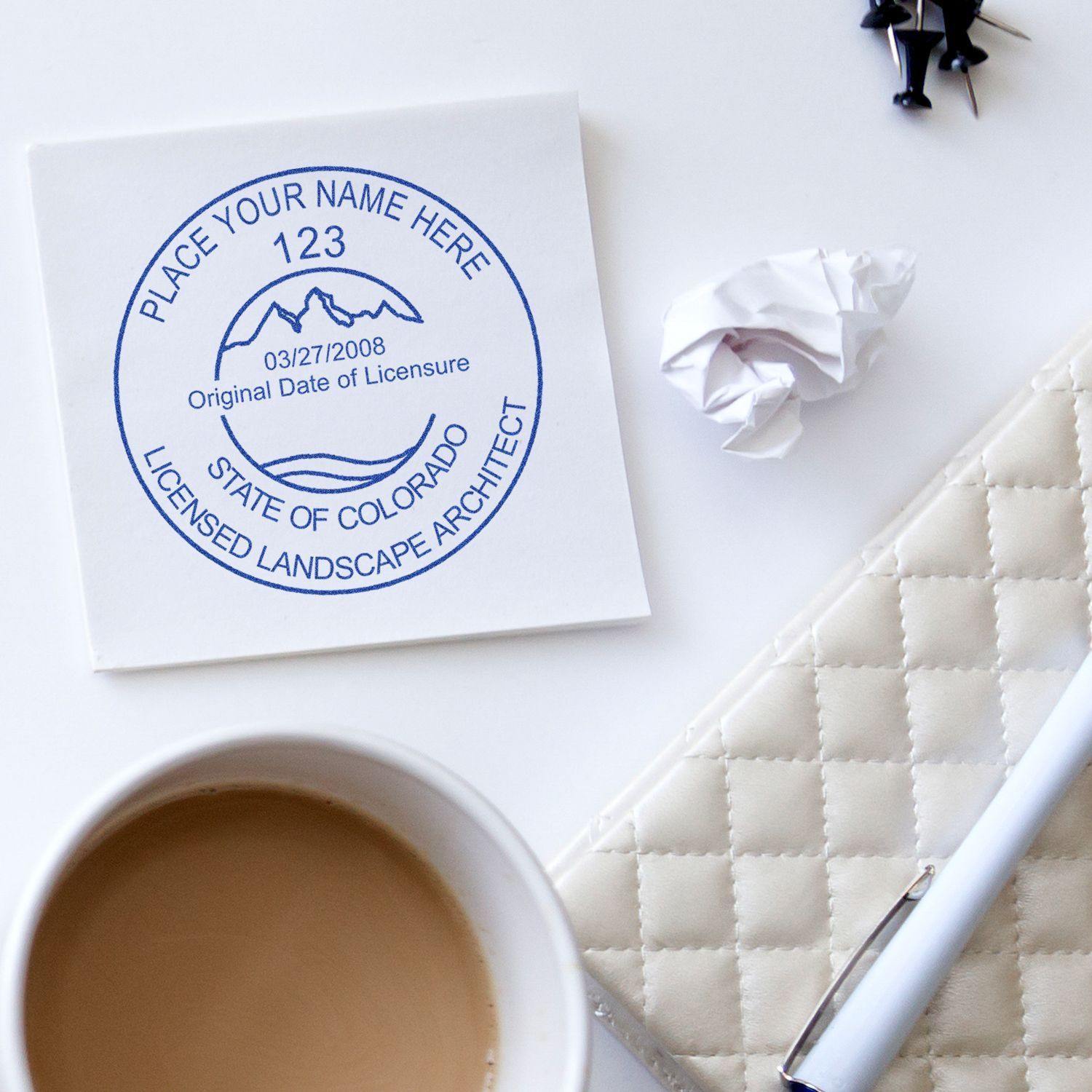 Landscape Architect MaxLight Pre Inked Rubber Stamp of Seal in use on a document, with a coffee cup, pen, and crumpled paper nearby.
