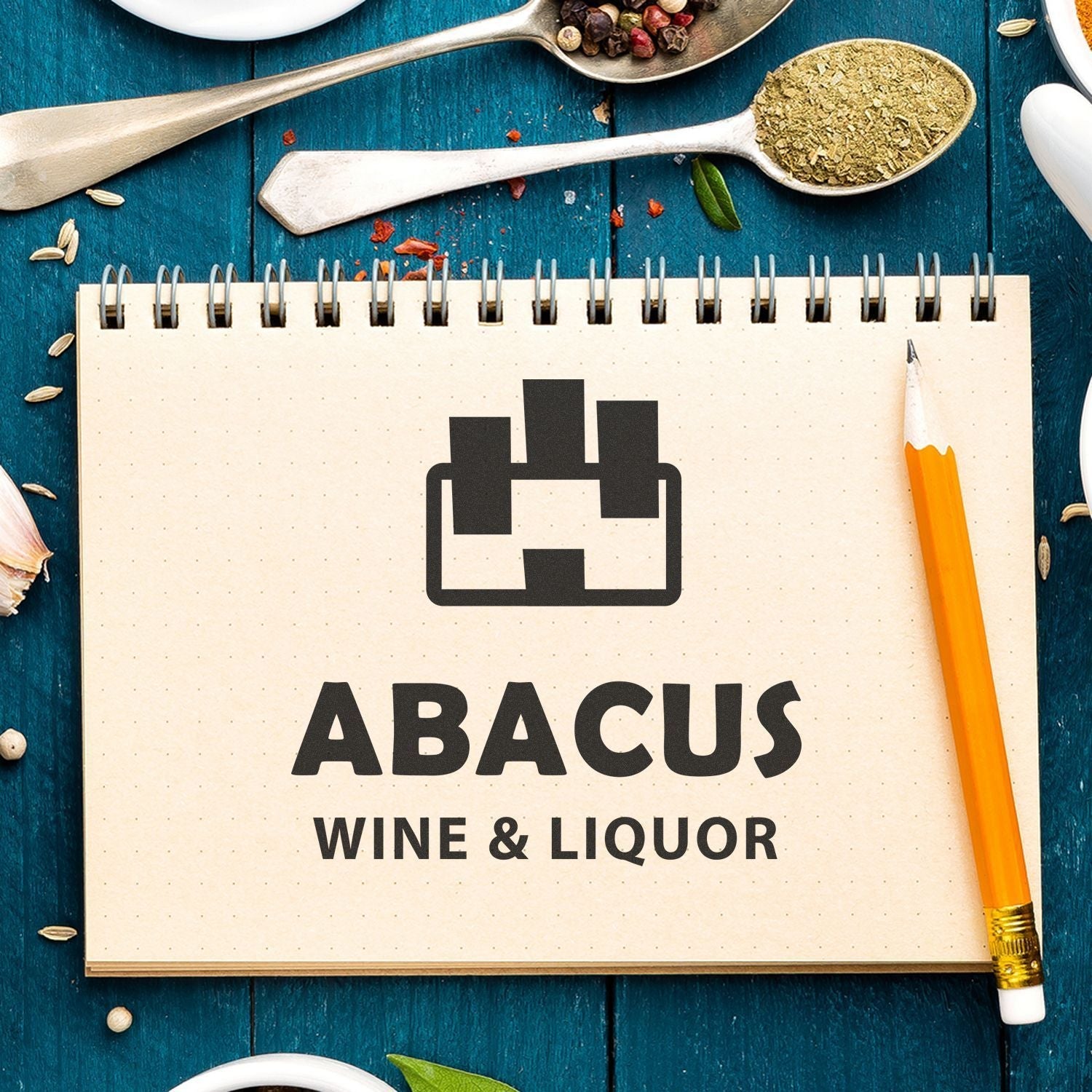 Custom Rubber Stamp Size 8 x 8 used on a notebook with ABACUS WINE & LIQUOR text, surrounded by a pencil and kitchen spices.
