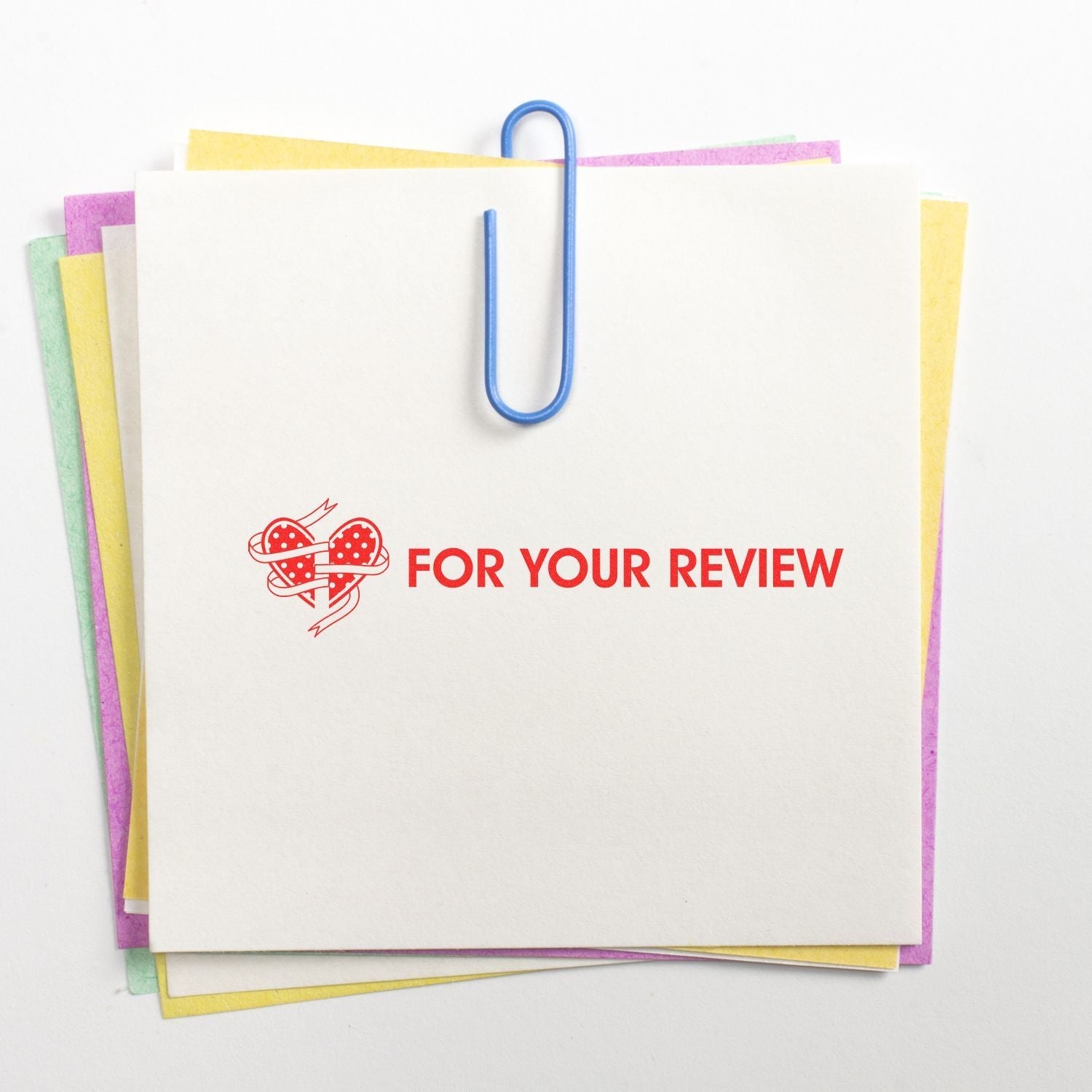 A stack of colorful papers with a blue paperclip, stamped with FOR YOUR REVIEW using the Super Slim 1442 Customized Pre-Inked Stamp 1/2 x 1-5/8.