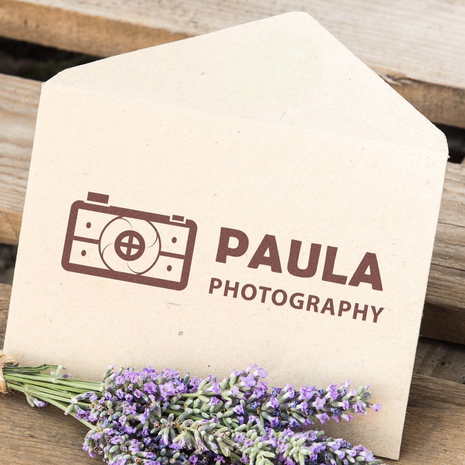 Envelope stamped with PAULA PHOTOGRAPHY using Custom Rubber Stamp Size 1-1/2 x 6, placed on wooden surface with lavender flowers.