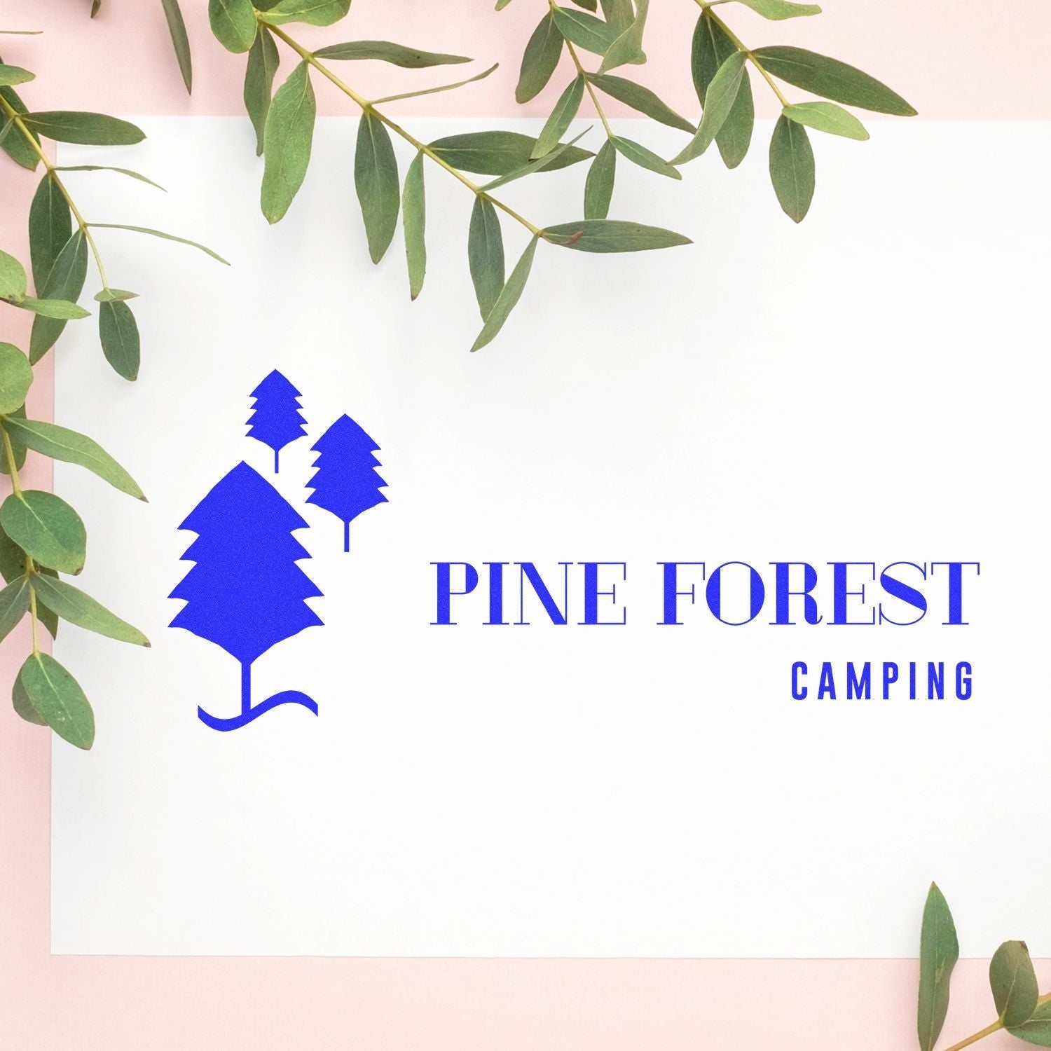 Custom Rubber Stamp Size 6 x 10 used to create a blue Pine Forest Camping logo on white paper, surrounded by green leaves.