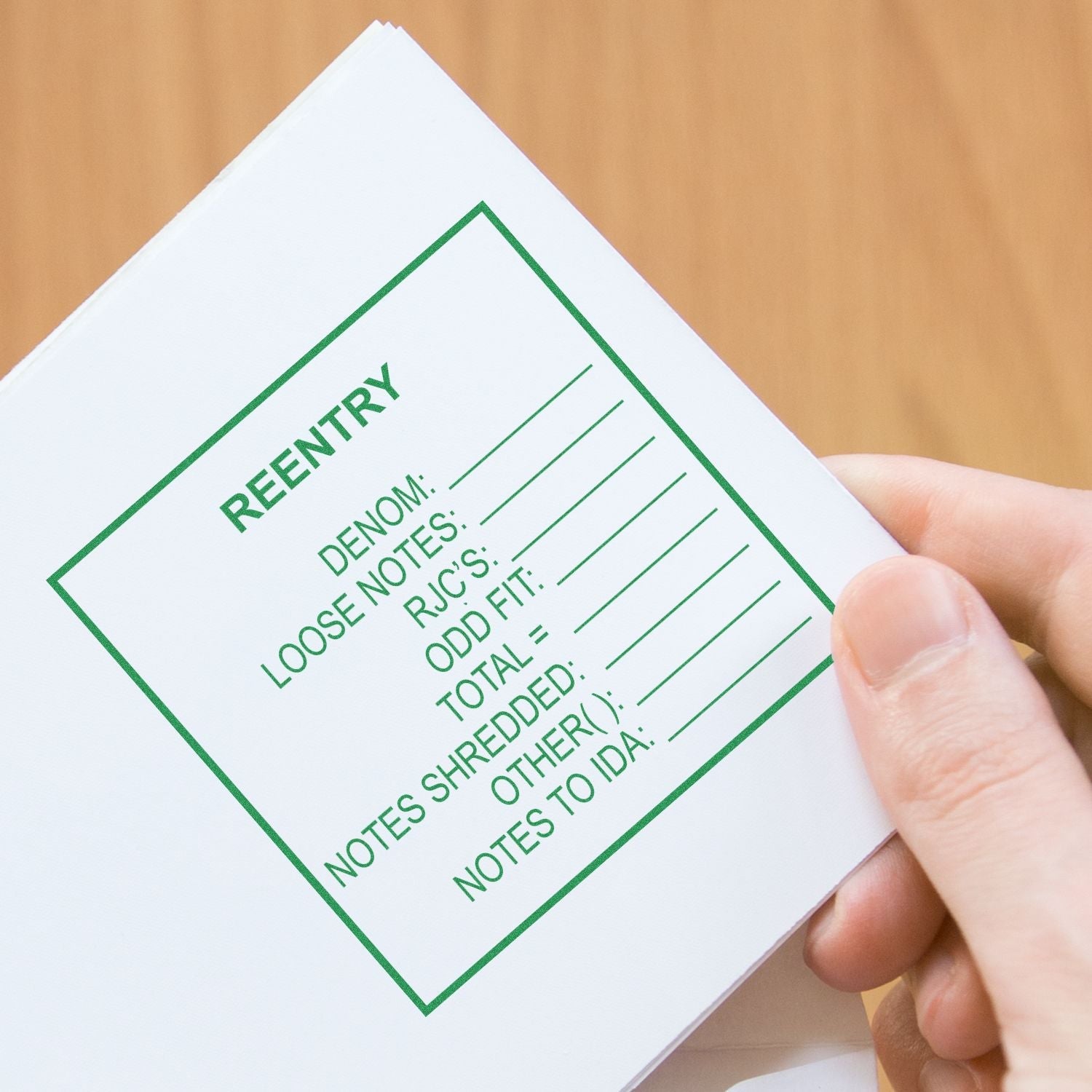 Hand holding a paper stamped with a green REENTRY form using a Custom Rubber Stamp Size 5 x 5 on a wooden surface.