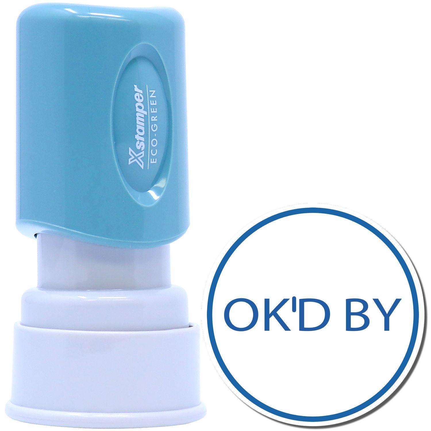Round OK'D By Xstamper Stamp with a blue handle and white base, next to a stamped impression reading OK'D BY in blue within a circle.