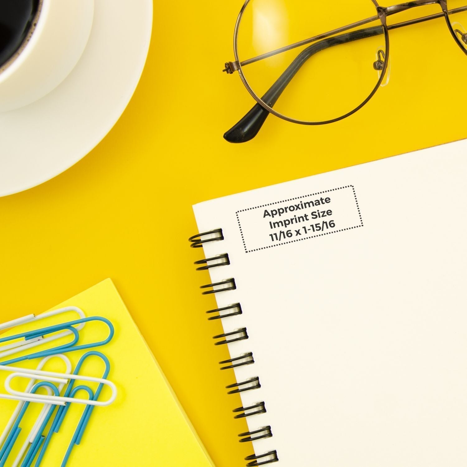 MaxLight XL2-42 Custom Pre-Inked Business Stamp 11/16 x 1-15/16 on a yellow desk with a notebook, glasses, coffee, and paperclips.