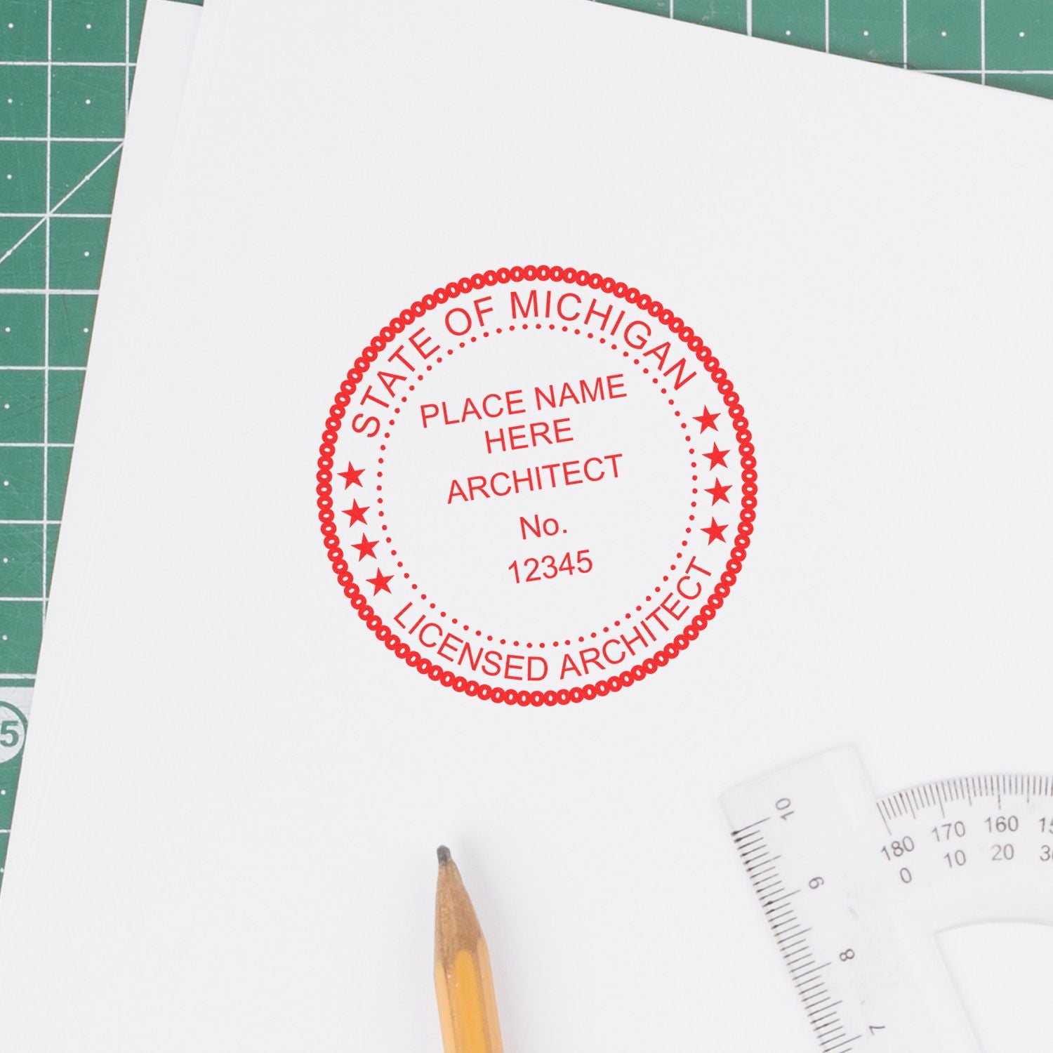 Self Inking Michigan Architect Stamp in red ink on white paper, placed on a green cutting mat with a pencil and ruler nearby.