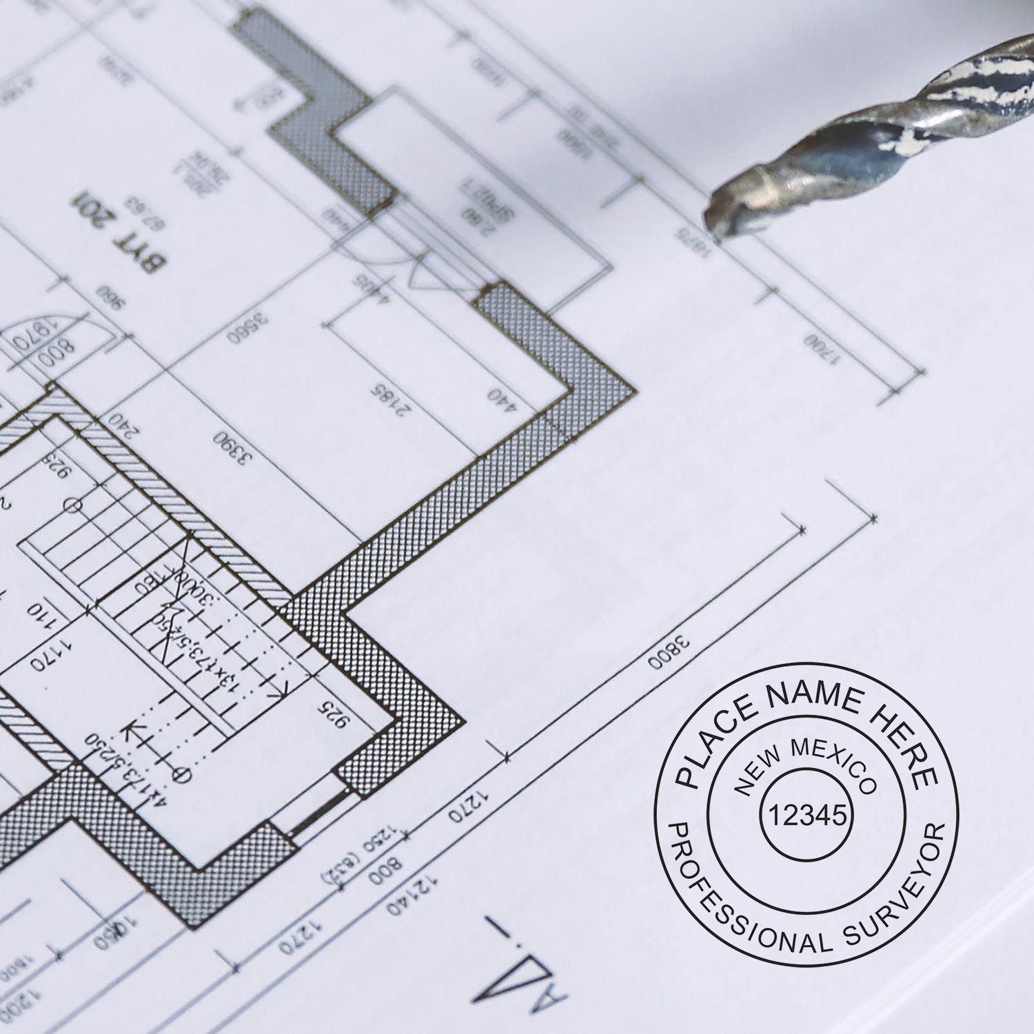Premium MaxLight Pre-Inked New Mexico Surveyors Stamp used on a detailed architectural blueprint with a drill bit nearby.