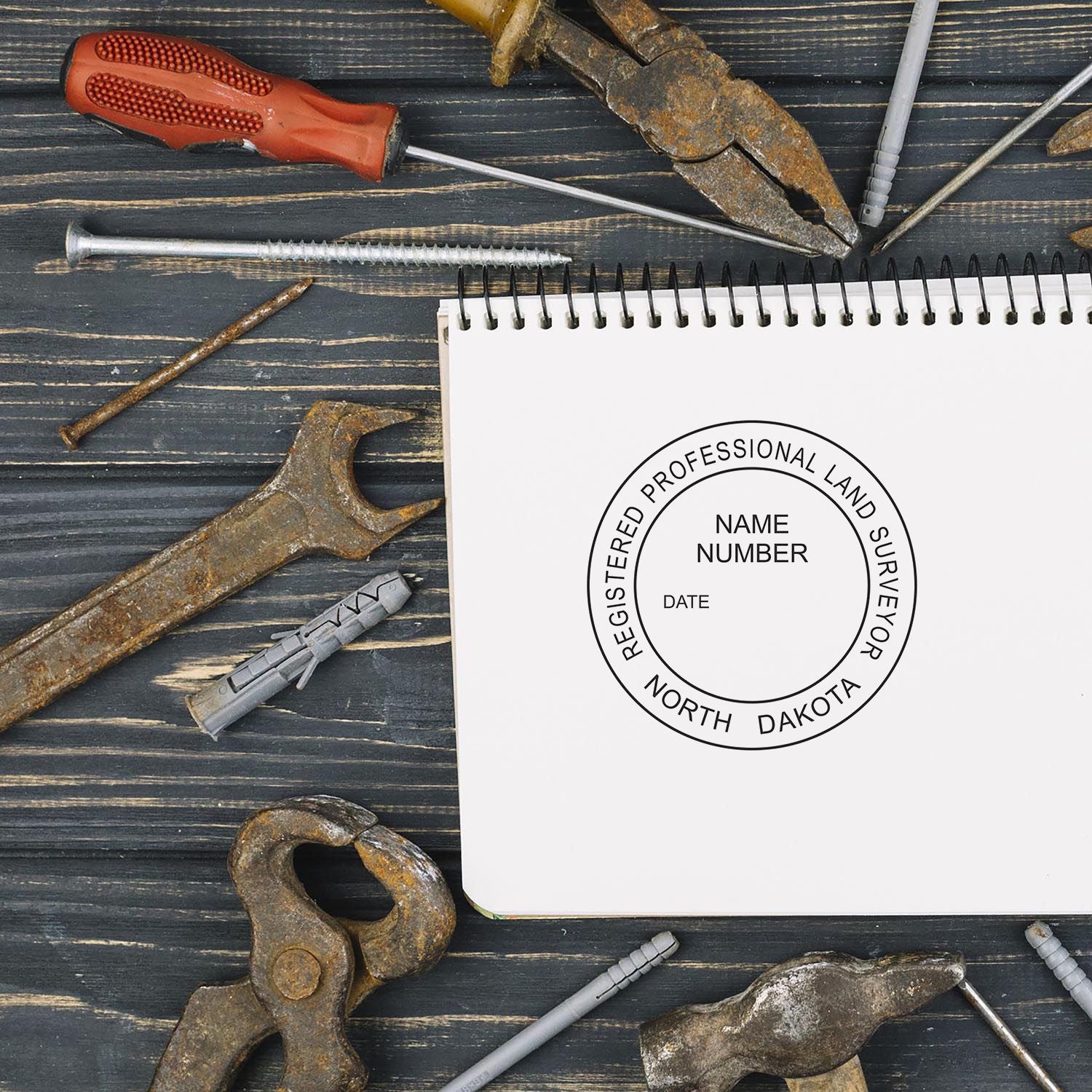 North Dakota Land Surveyor Seal Stamp on a notebook surrounded by various tools on a wooden surface.